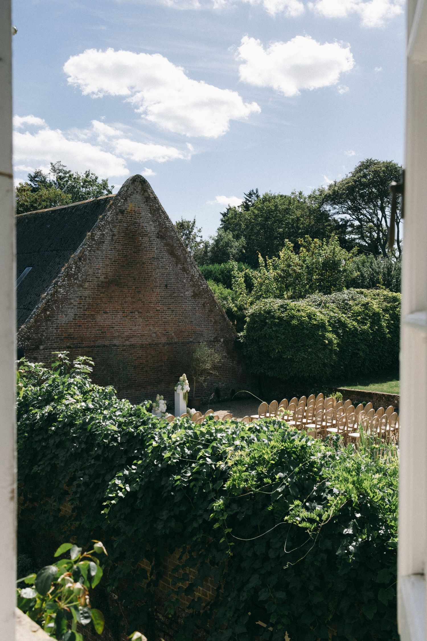 Lush green garden with ivy-covered walls, rustic brick structure, and rows of chairs under a blue sky.