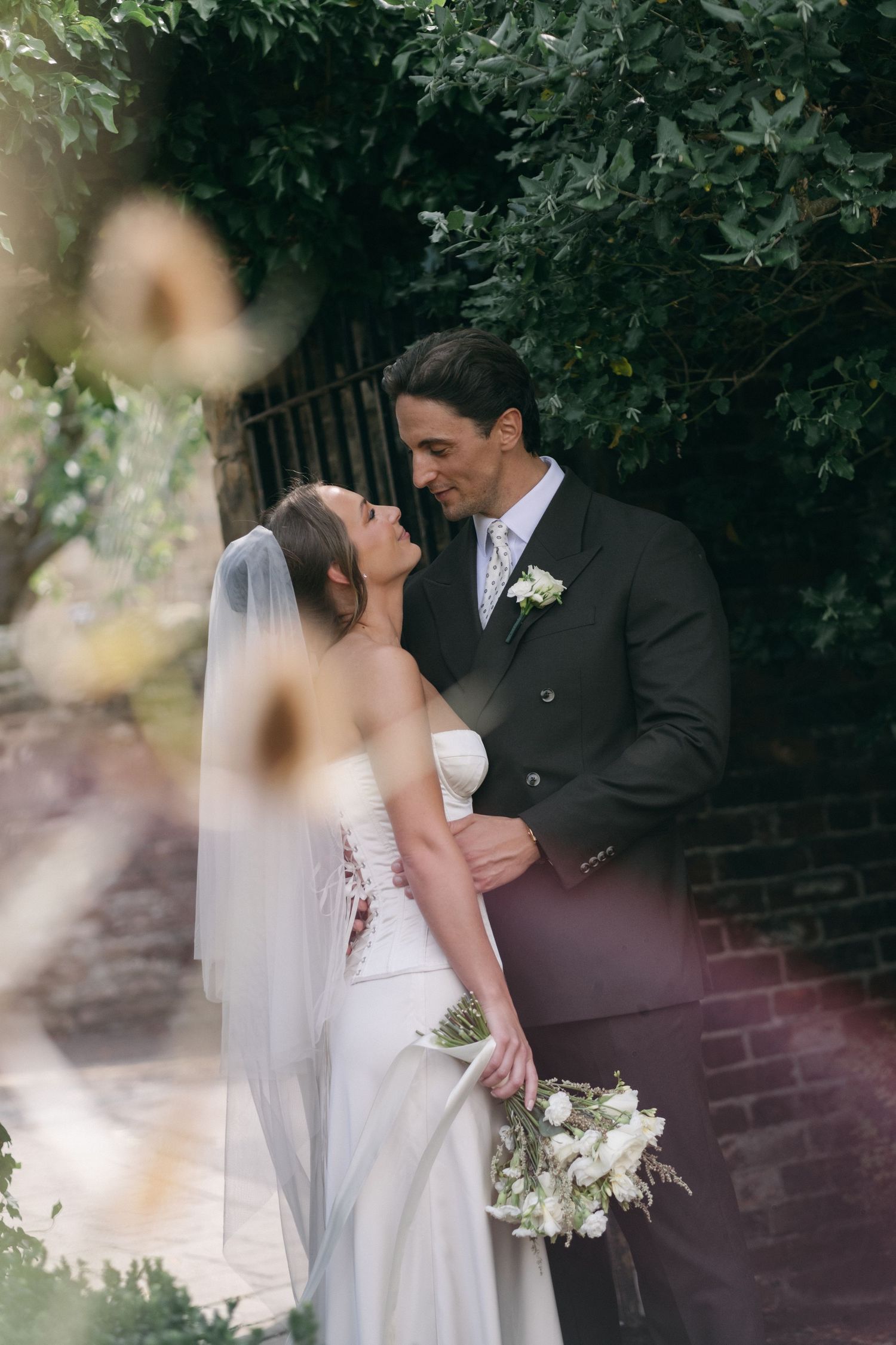 Bride and groom share romantic moment outdoors, bride in white gown with veil holding white bouquet.