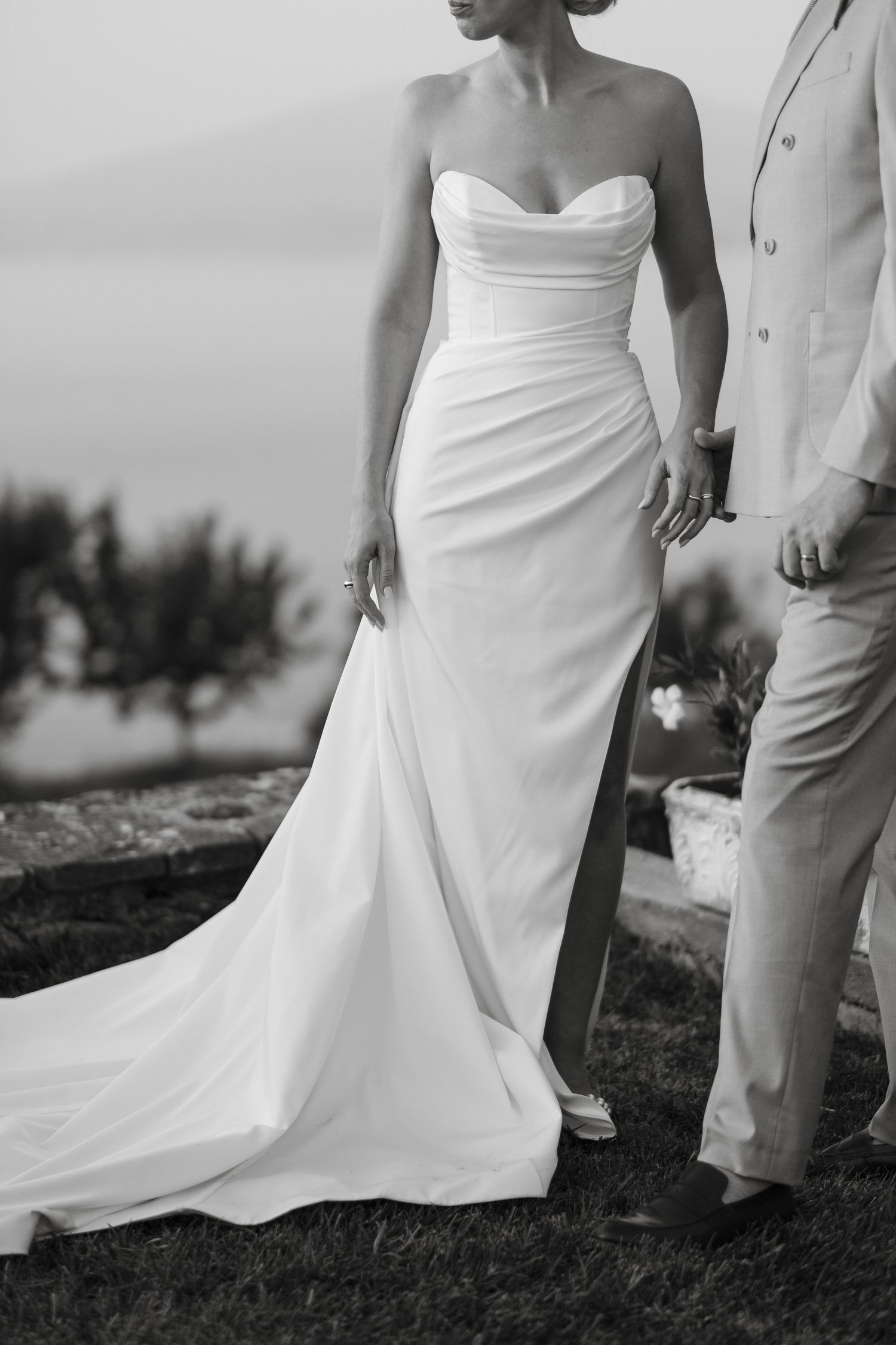 Black and white close-up of bride in elegant strapless ruched wedding gown with a flowing train.