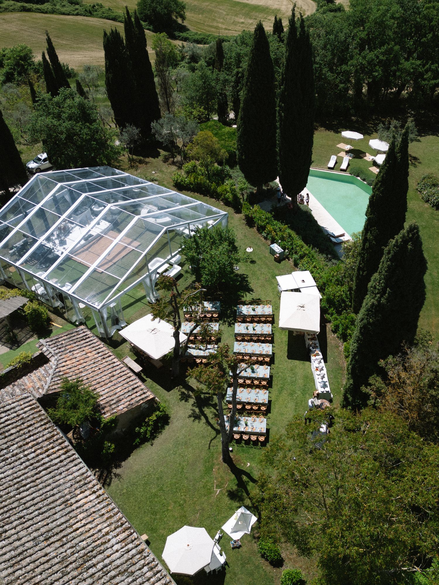 Aerial view of Tuscan villa with glass marquee, pool, and outdoor dining tables.