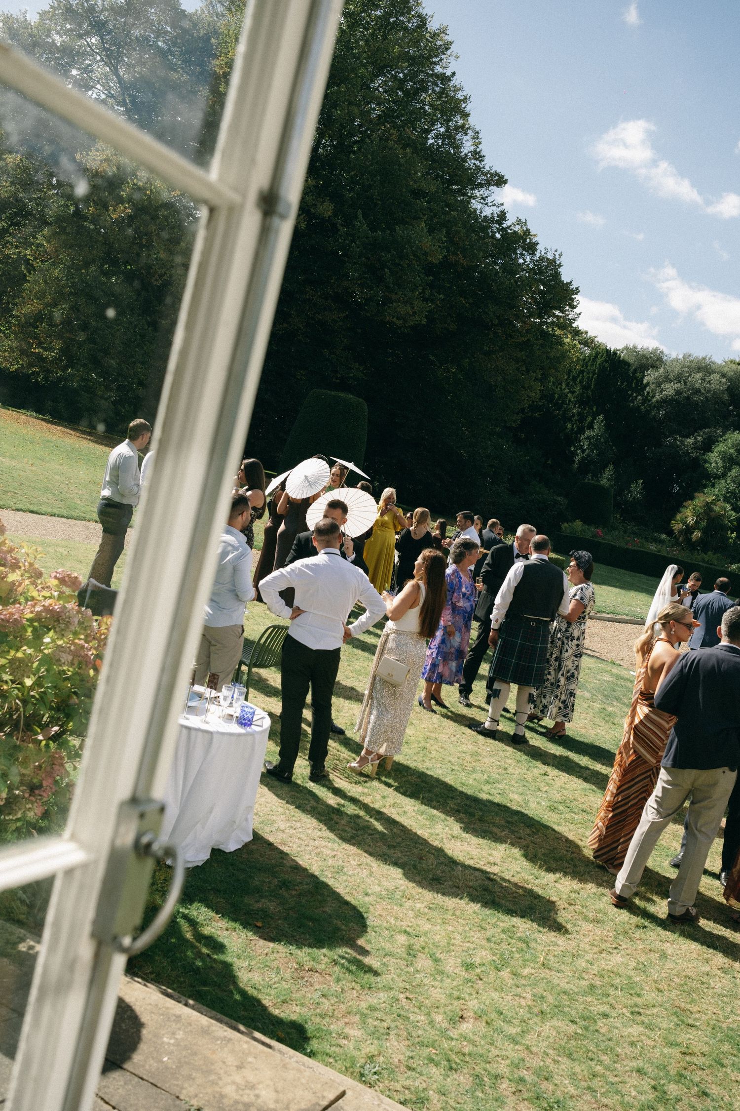 Guests gathered outdoors on a sunny day at an elegant garden wedding reception on a lush green lawn.