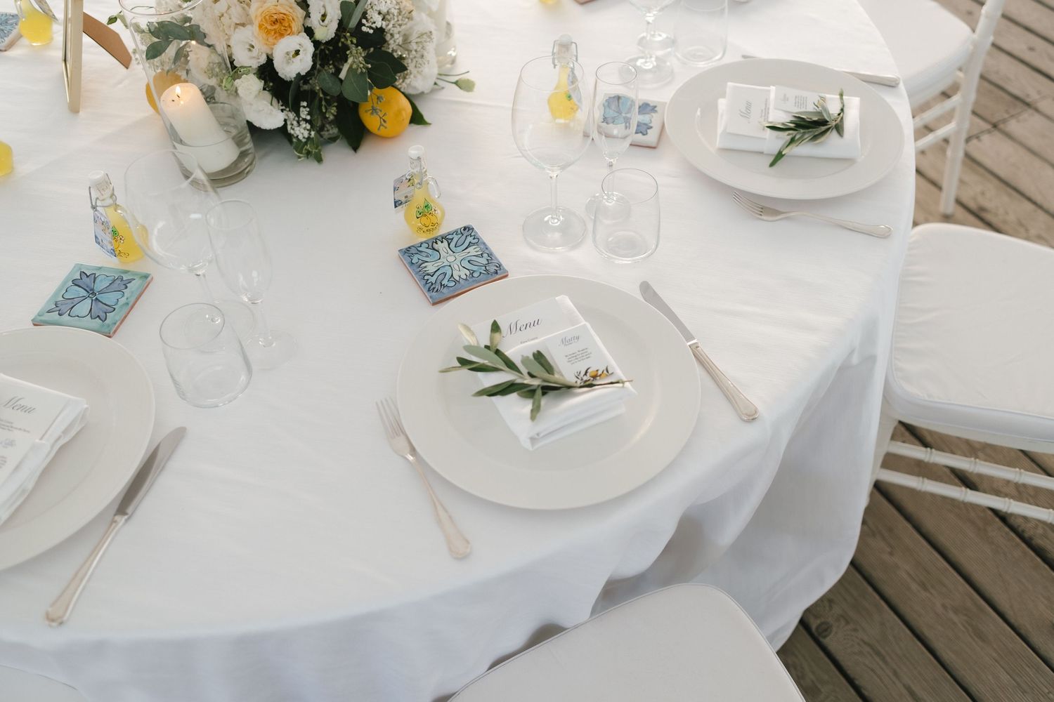 Elegant white wedding reception table setting with blue tile place cards and yellow floral centerpiece.