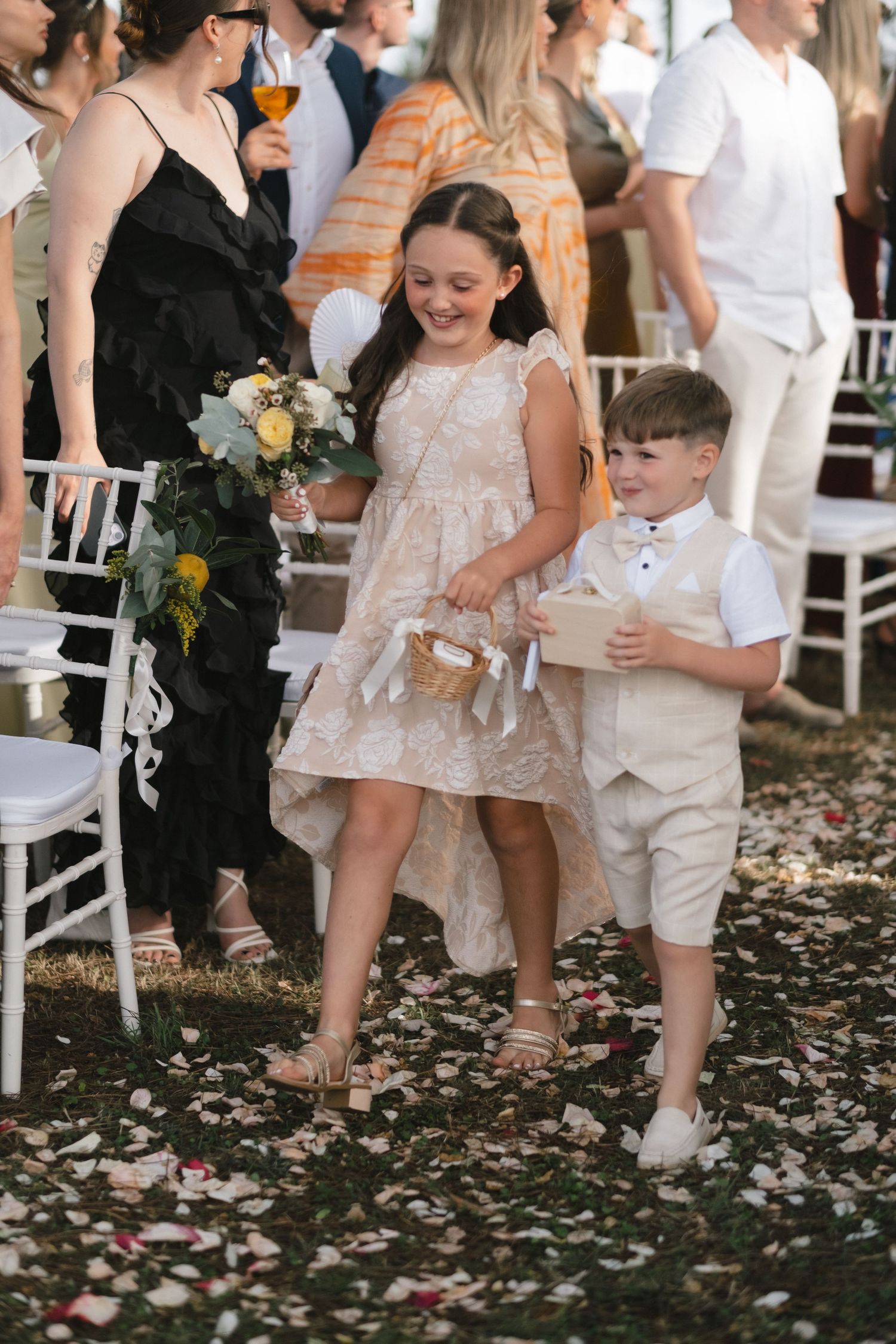 Smiling flower girl and ring bearer walking down petal-strewn wedding aisle.