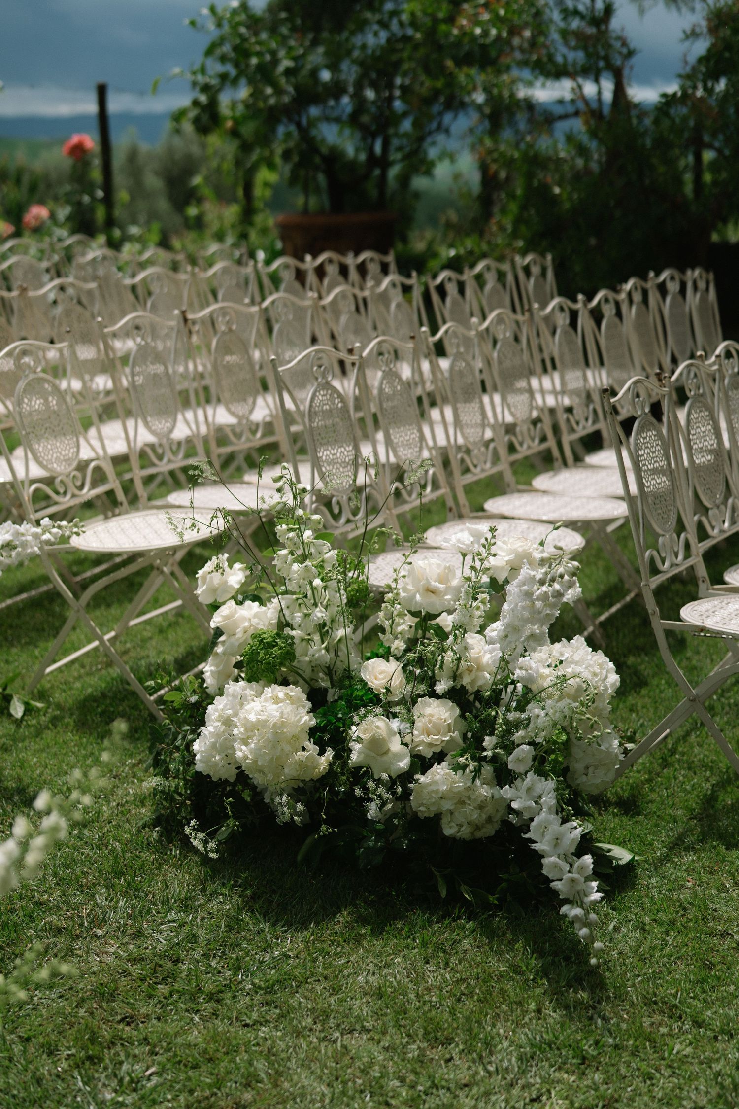 Elegant white flower bouquet with peonies and greenery placed beside white chairs at an outdoor garden wedding ceremony.