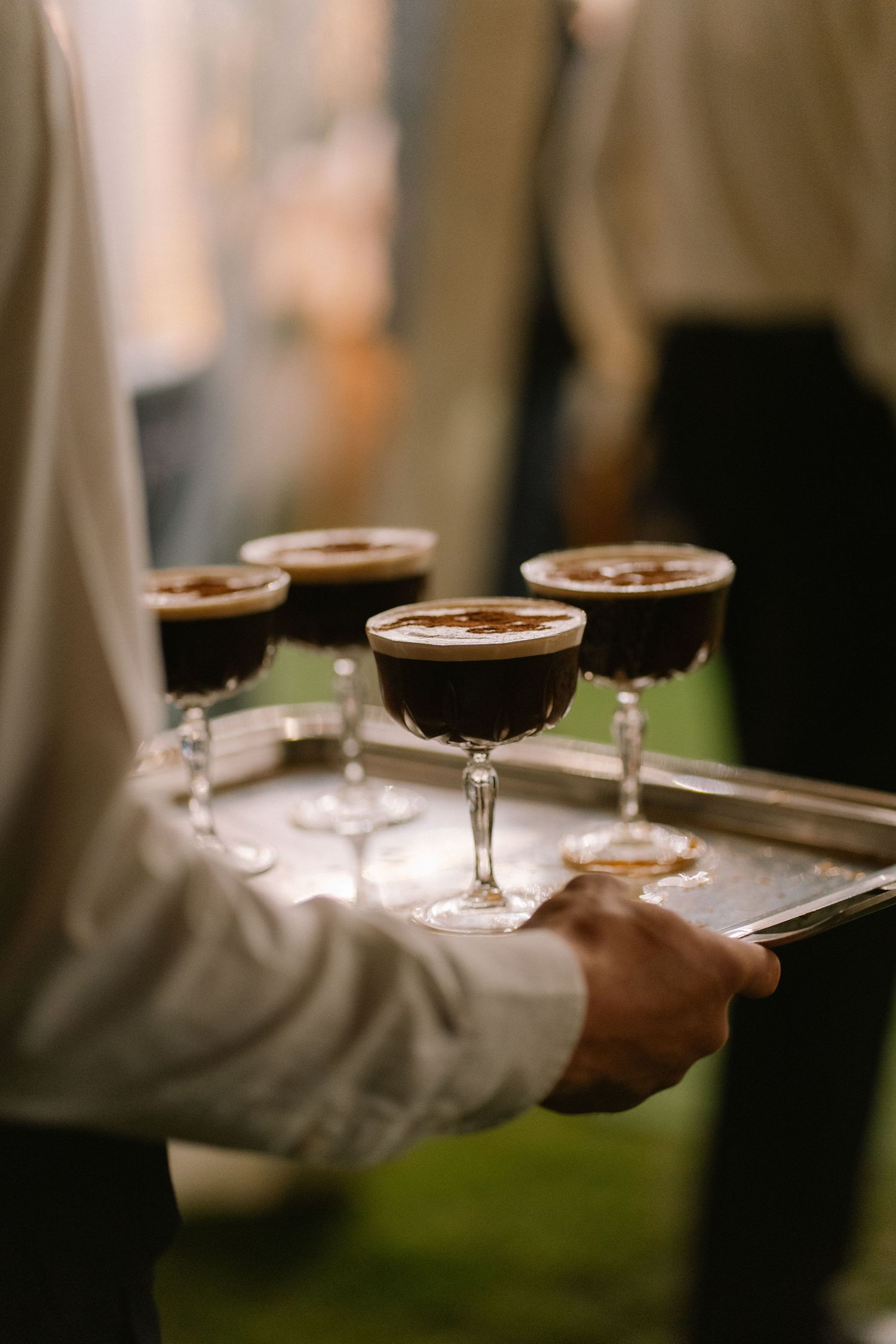Waiter serving espresso martini cocktails on a silver tray at an elegant wedding reception.