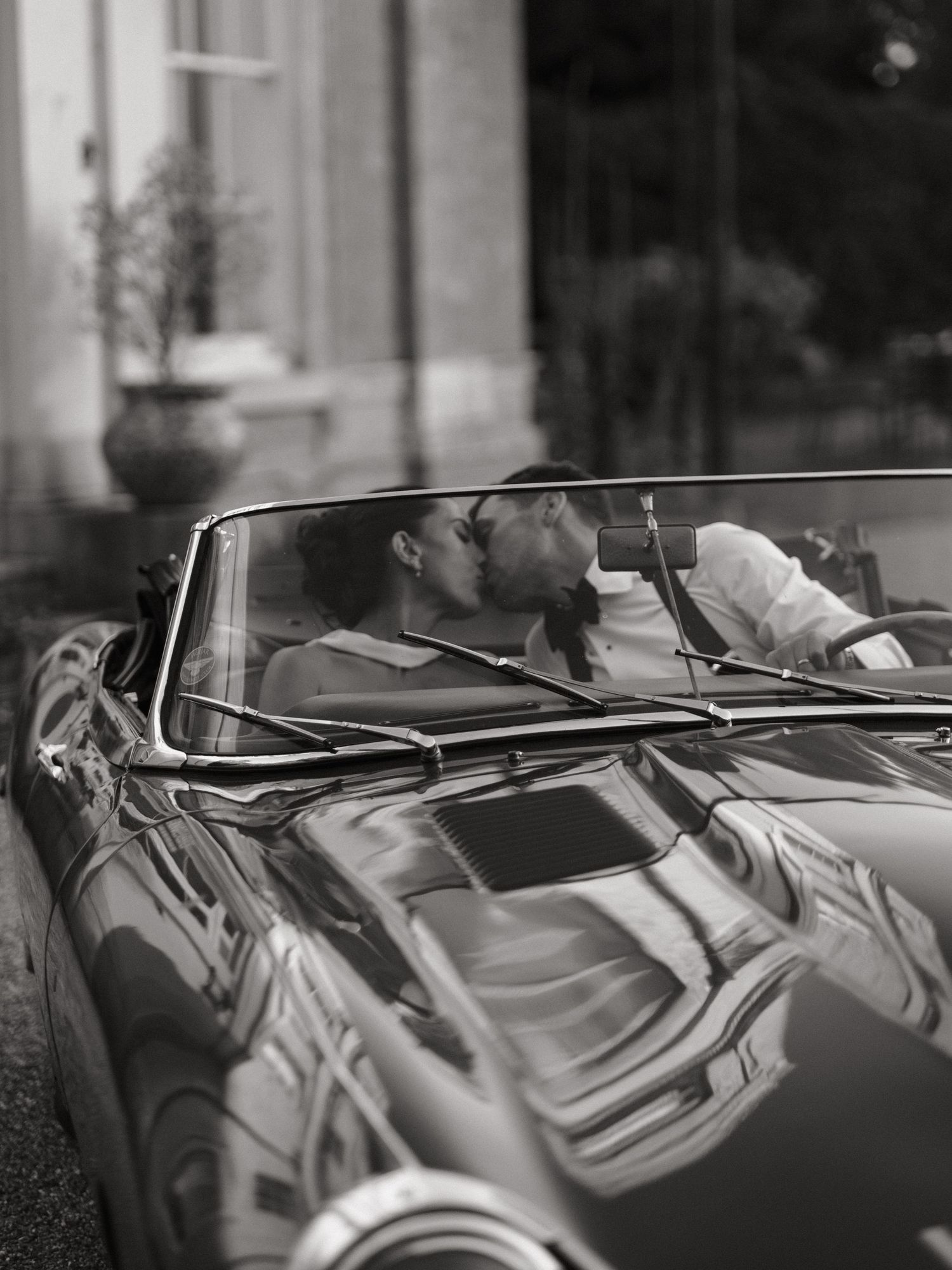 A couple shares a romantic kiss in a classic convertible car, captured in elegant black and white photography.