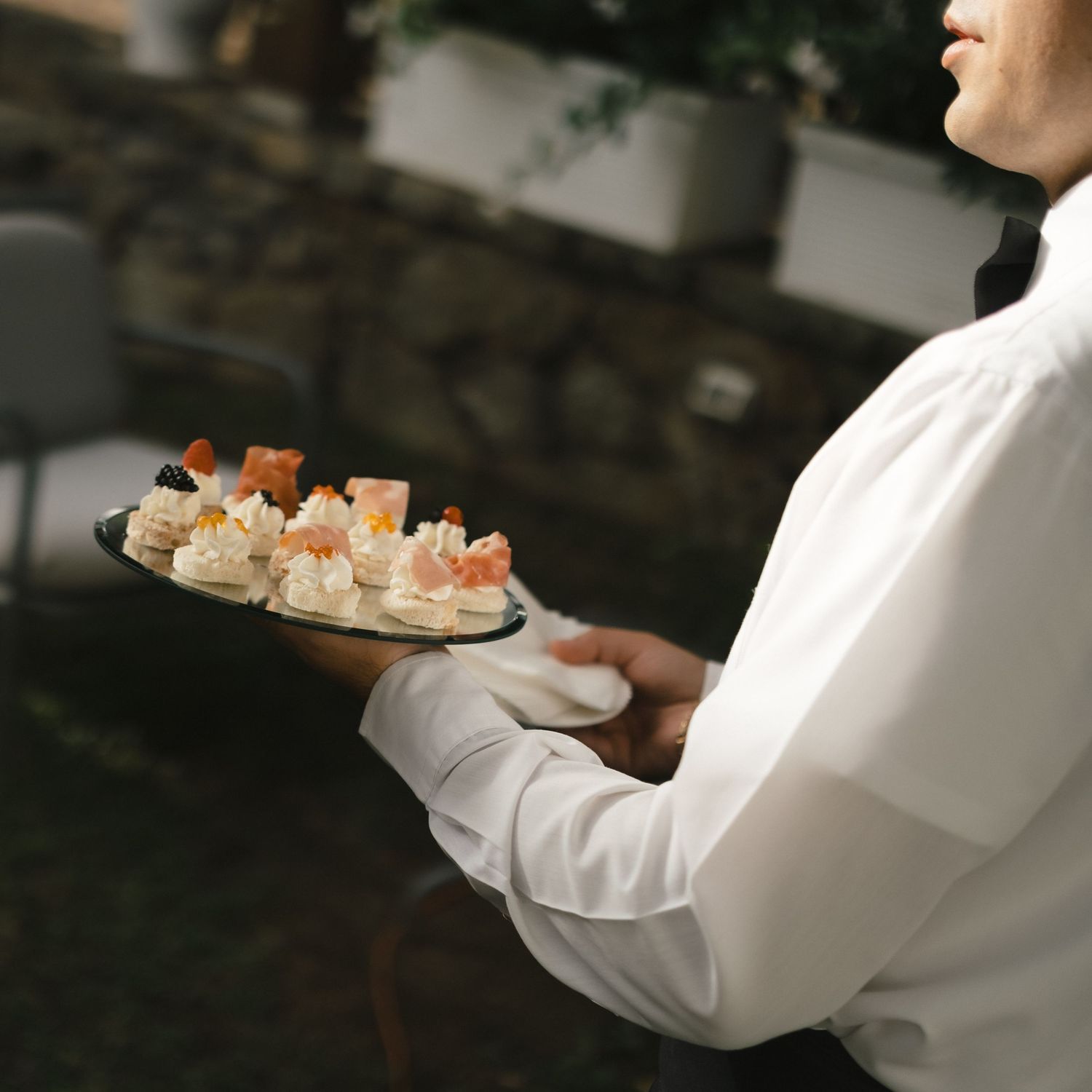 Waiter in white uniform holding a tray of elegant appetizers and canapes at a catered event.