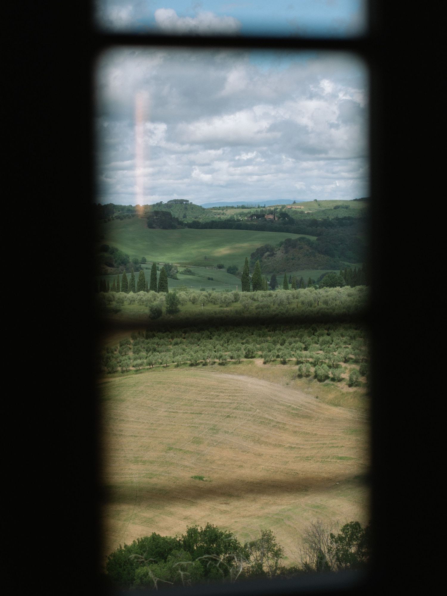 Rolling Tuscan countryside hills with cypress trees viewed through a rustic window frame.
