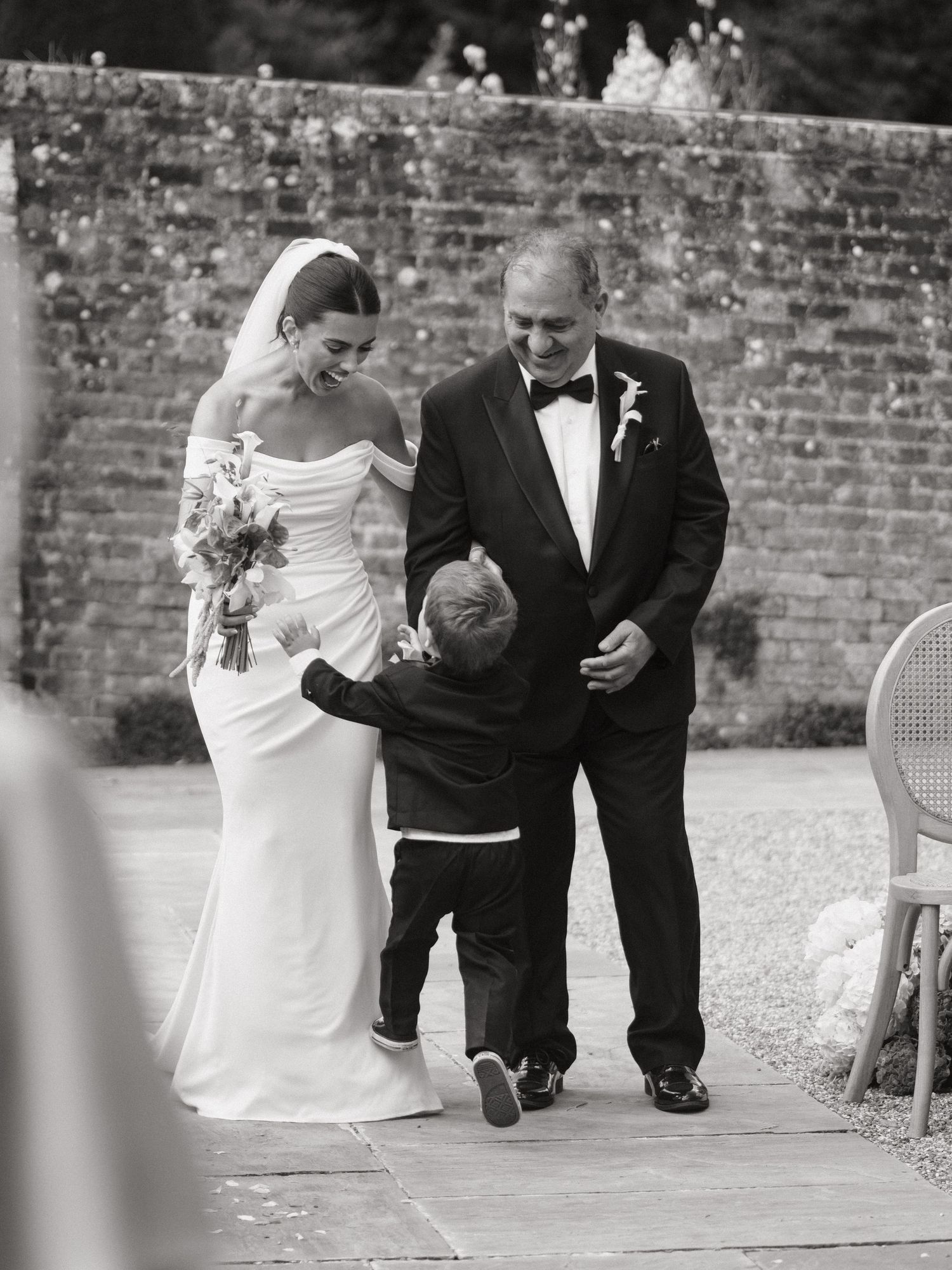 Black and white wedding photo of bride in off-shoulder gown, groom in tuxedo, and small child between them.