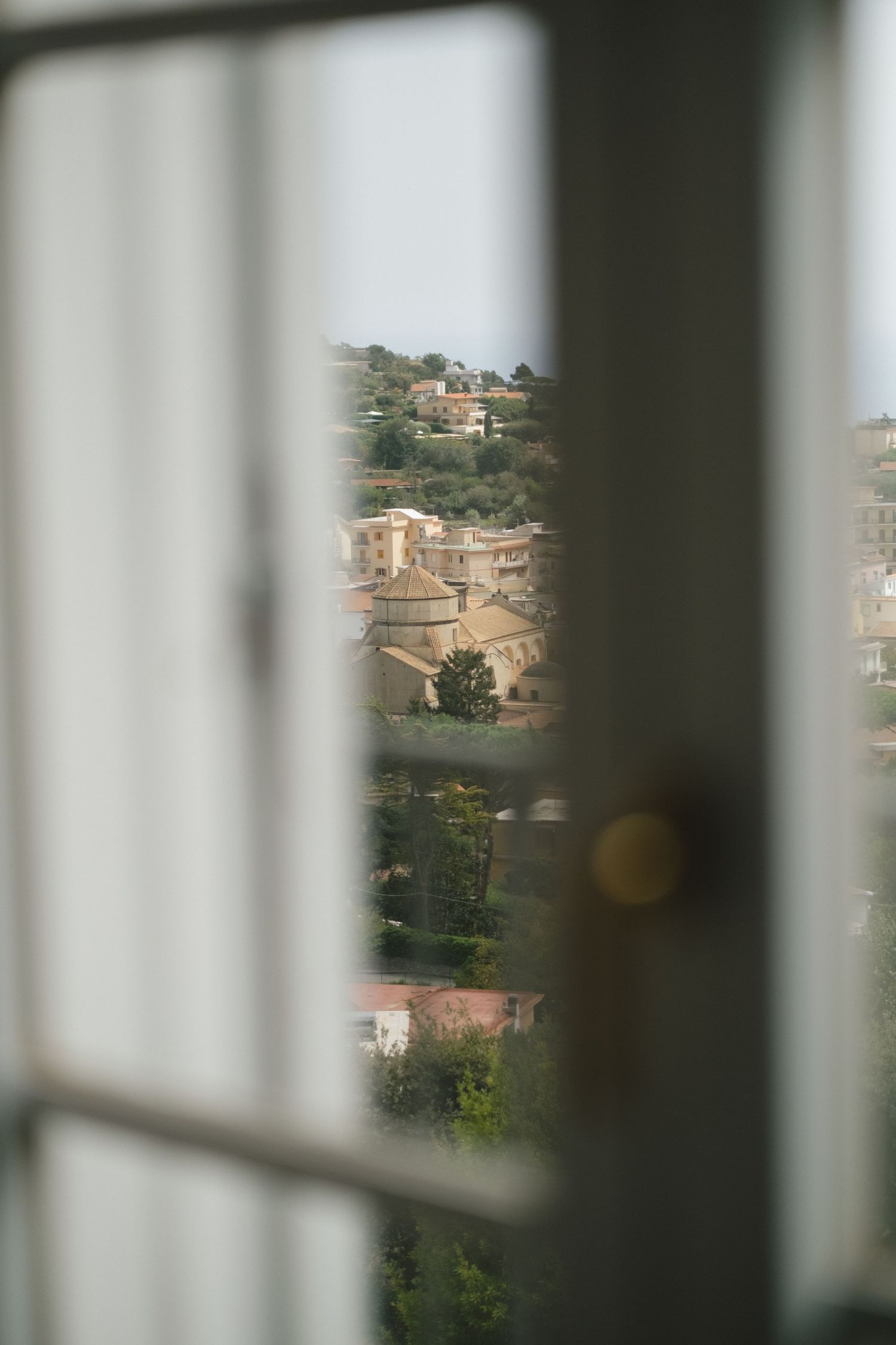 View through white window frame of a Mediterranean hillside town with historic domed building and terracotta rooftops.