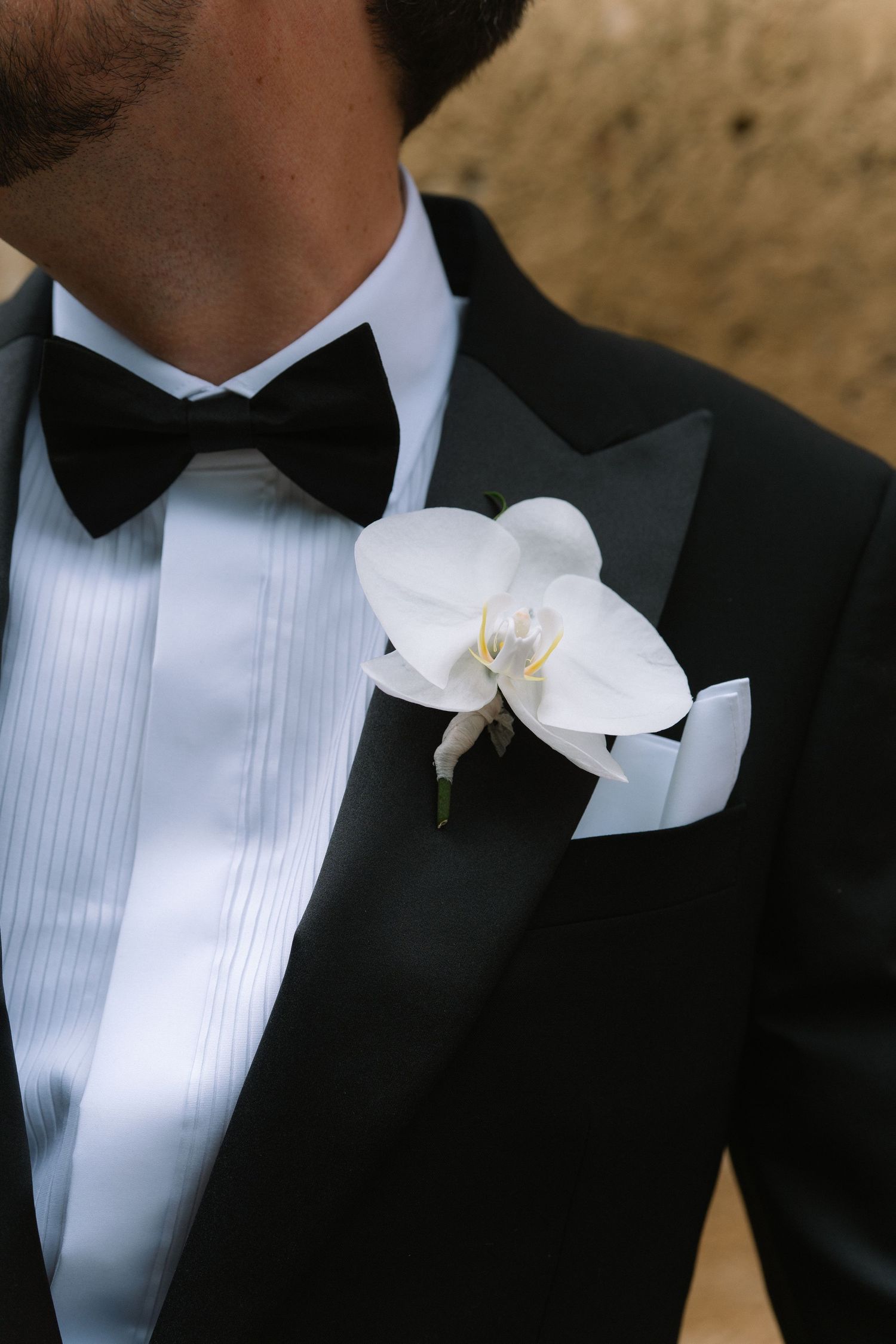 Groom wearing black tuxedo with bow tie, white orchid boutonniere, and pocket square.