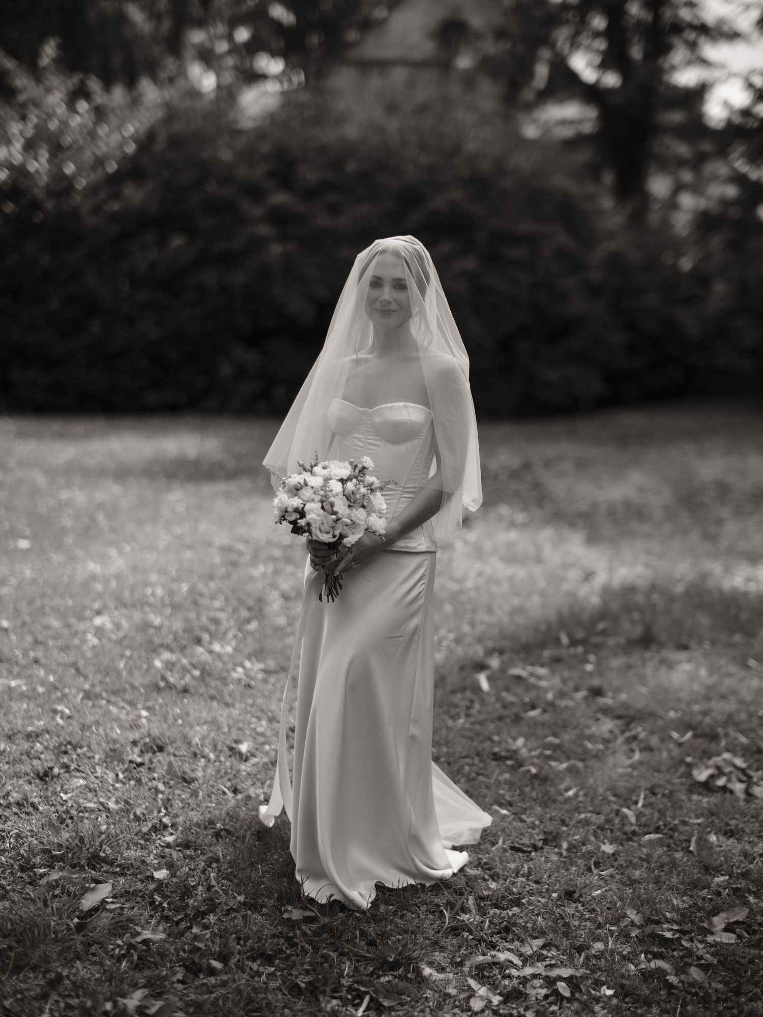Black and white portrait of a bride in a strapless gown and veil holding a bouquet outdoors.