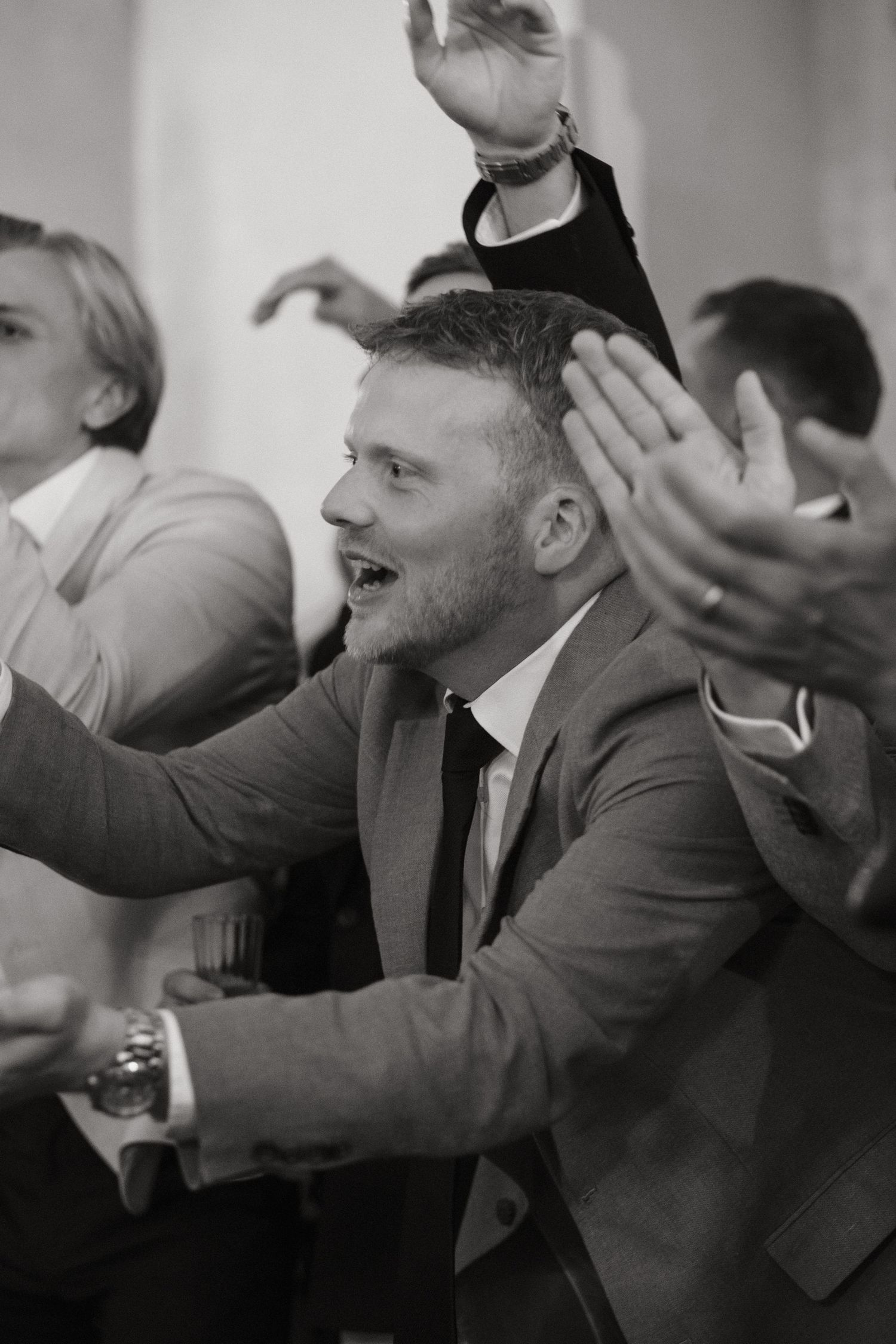 Black and white photo of a man in a suit clapping and smiling at a formal event surrounded by others.