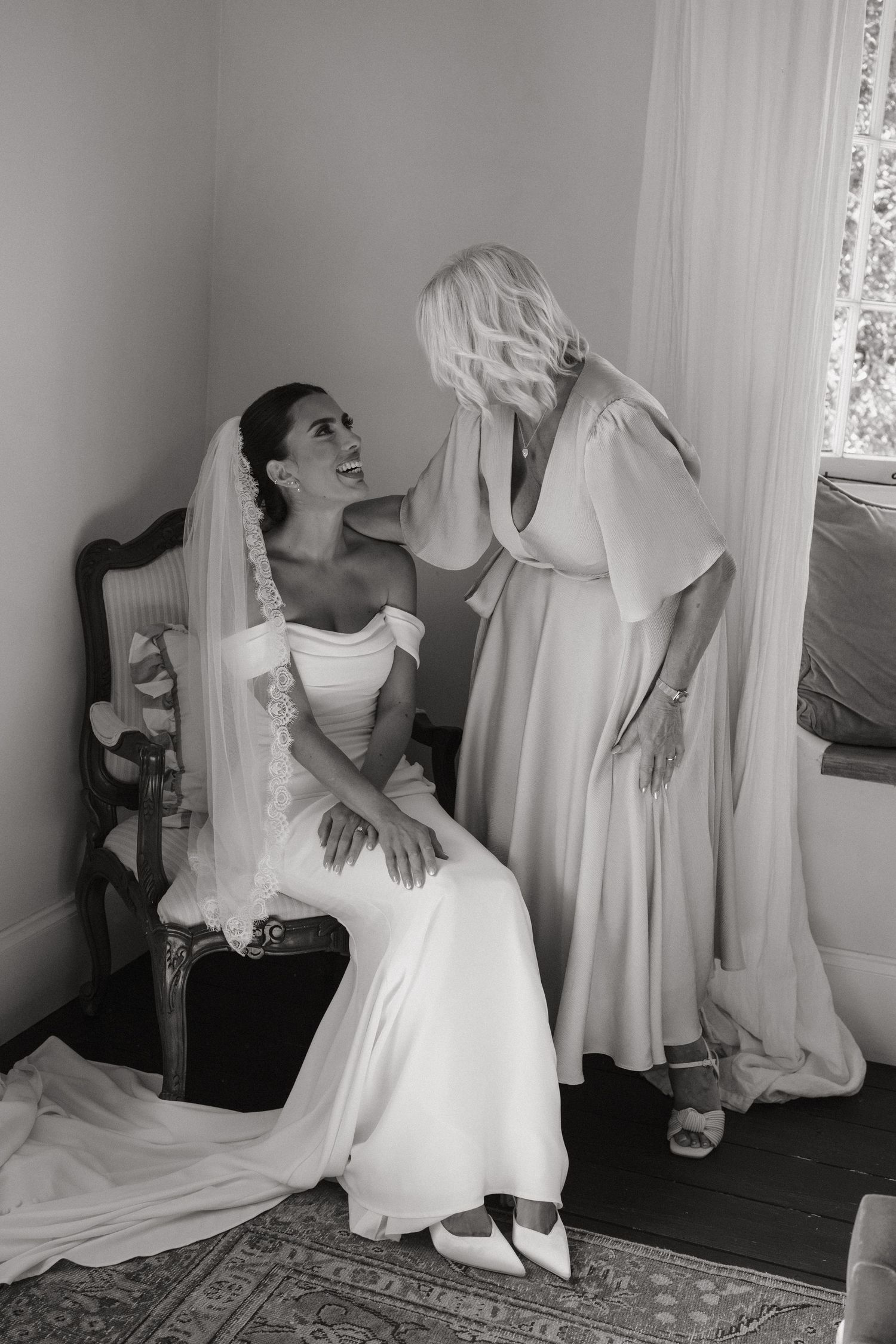 Black and white photo of a bride in a wedding gown and veil sharing an emotional moment with a bridesmaid.