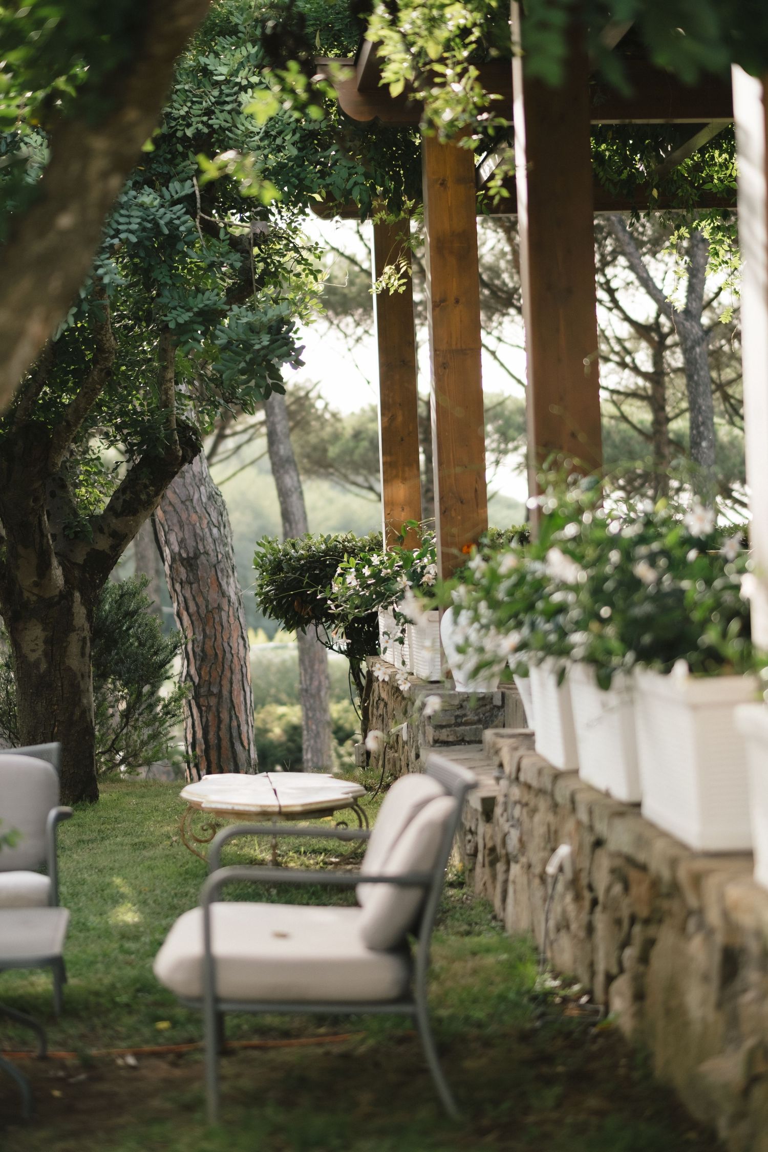 Elegant outdoor garden seating area with white chairs, stone wall planters, and lush green trees at a luxury venue.