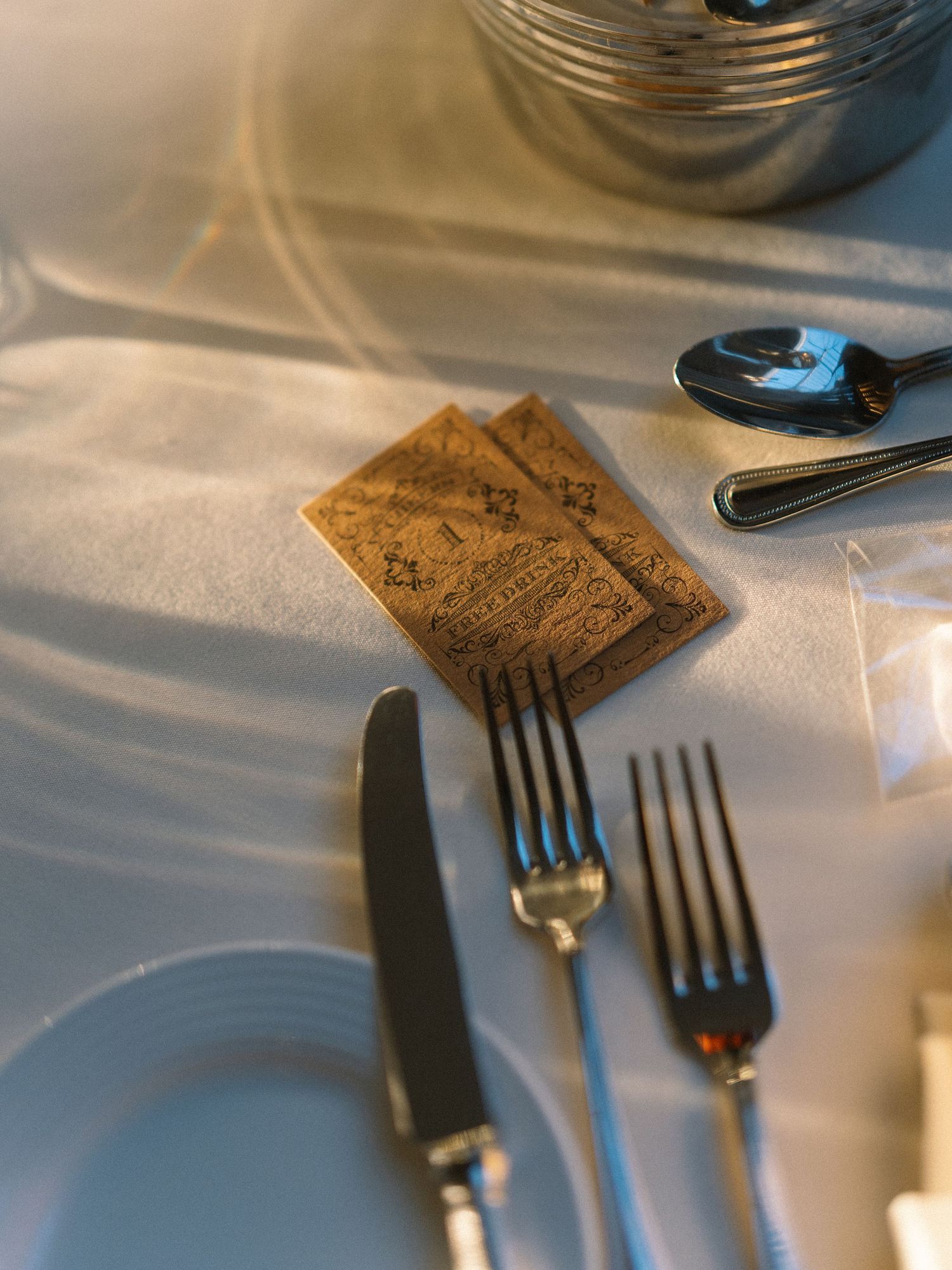 Elegant table setting with silver forks, knife, spoons, and vintage paper cards on a white linen tablecloth.