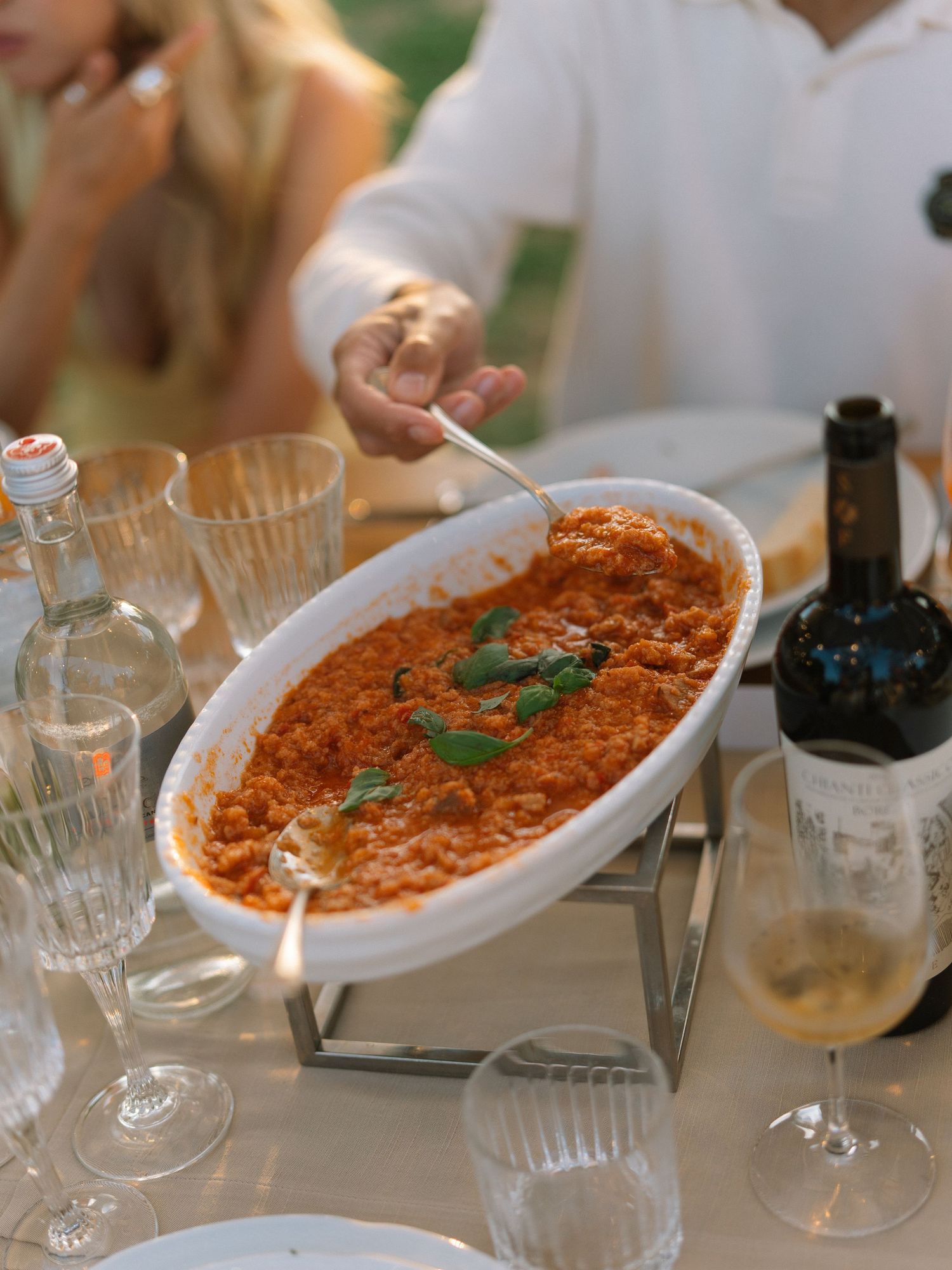 A serving dish of rich tomato pasta garnished with fresh basil at an outdoor Italian wedding reception table.