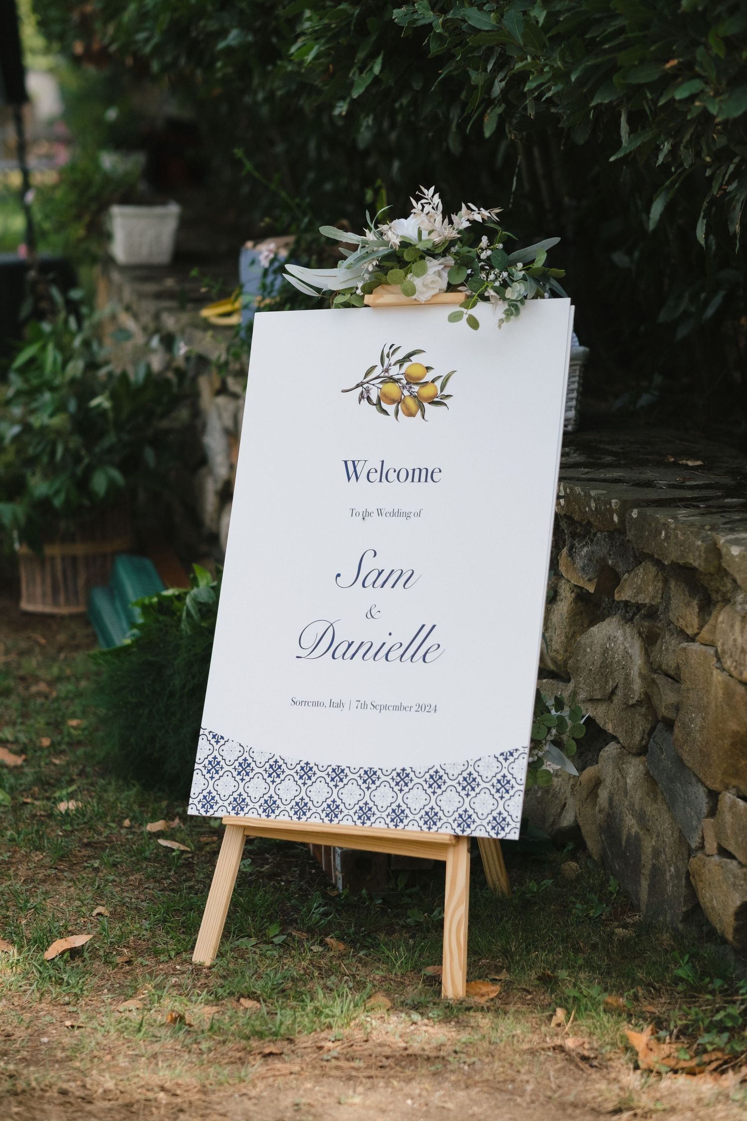 Wedding welcome sign for Sam & Danielle on wooden easel, decorated with lemon botanical motif and blue tile border pattern.