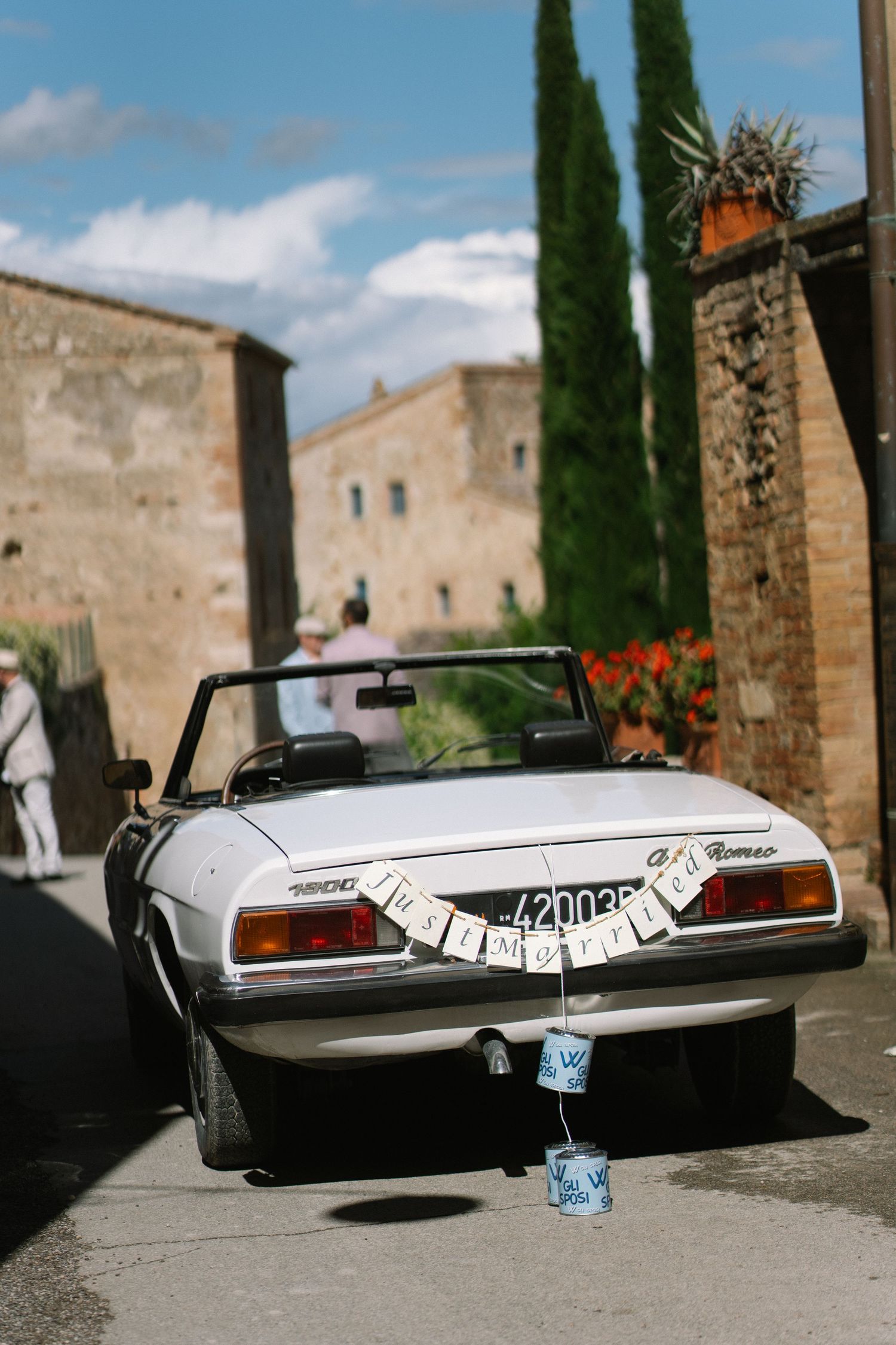 White vintage Alfa Romeo Spider wedding car decorated with tin cans and banners on a Tuscan village street.