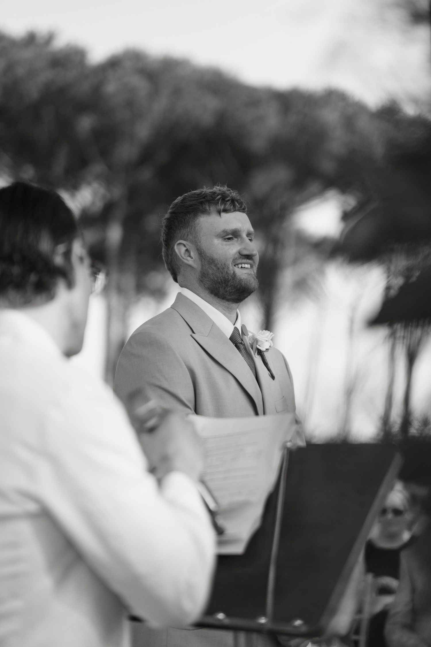 Black and white portrait of bearded groom smiling during outdoor wedding ceremony vows.