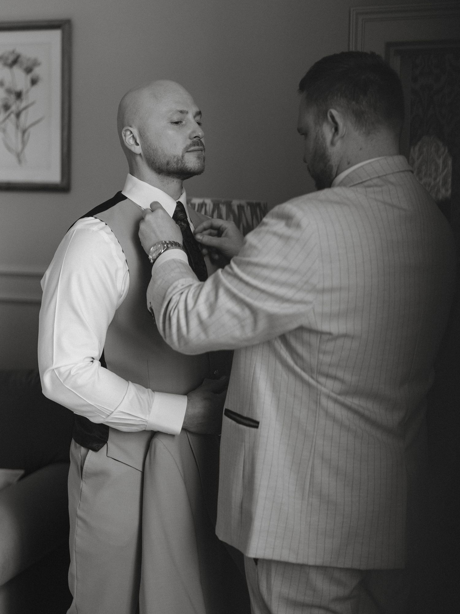 Black and white photo of a man adjusting another mans tie during wedding preparations.