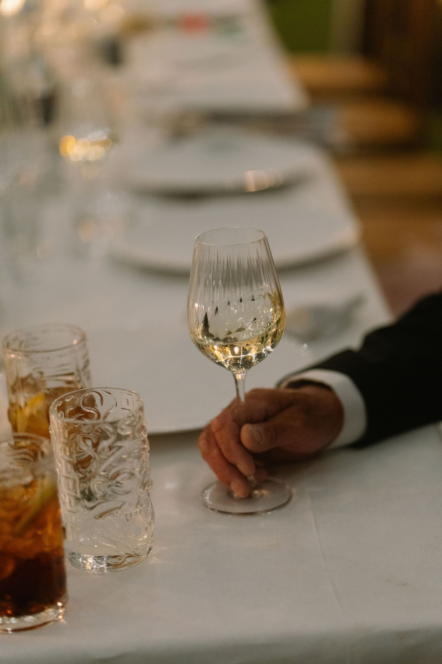 Close-up of a crystal wine glass held by a guest at a formal wedding dinner table.