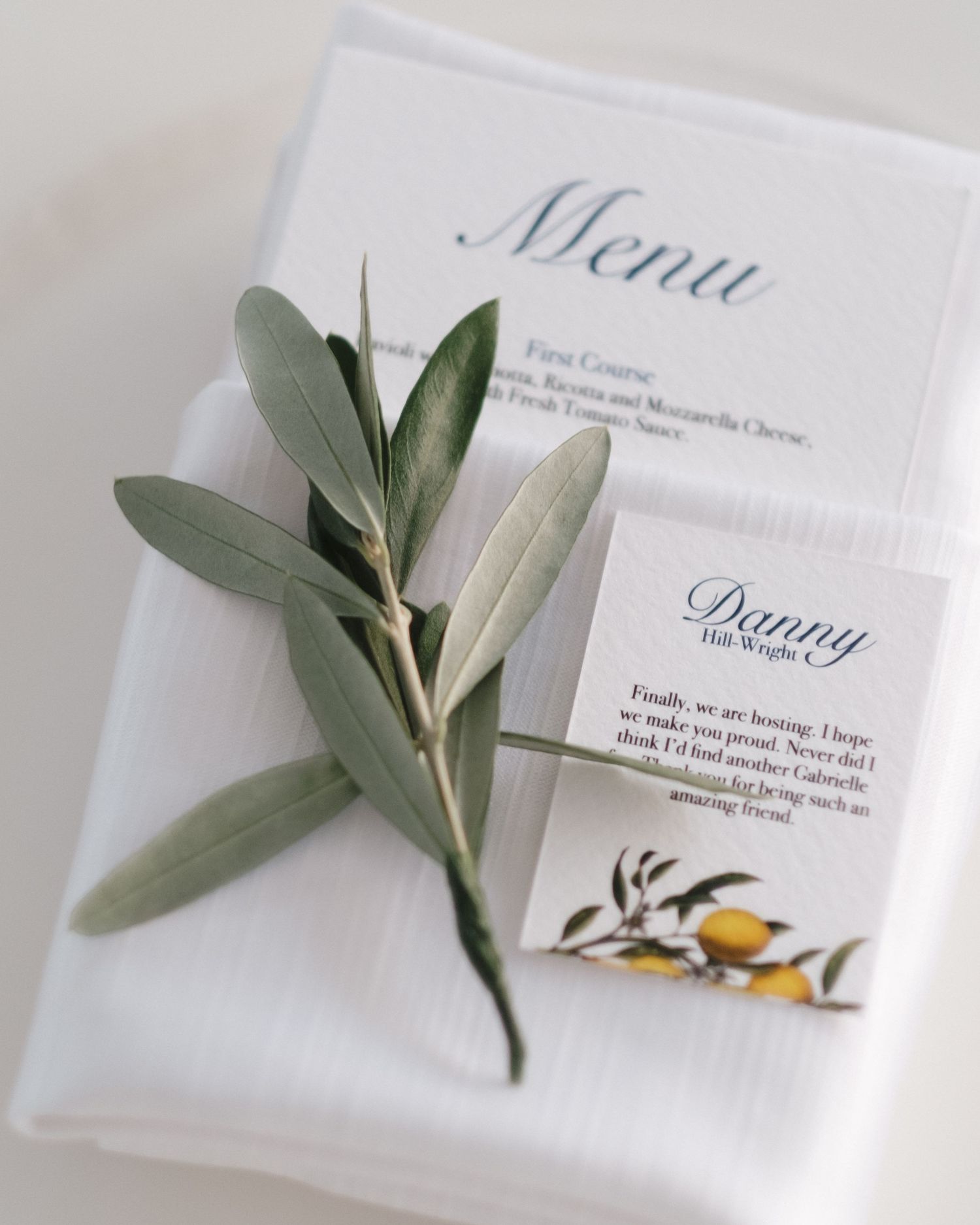 Wedding place card for Danny beside olive branch sprig on folded white linen menu card.