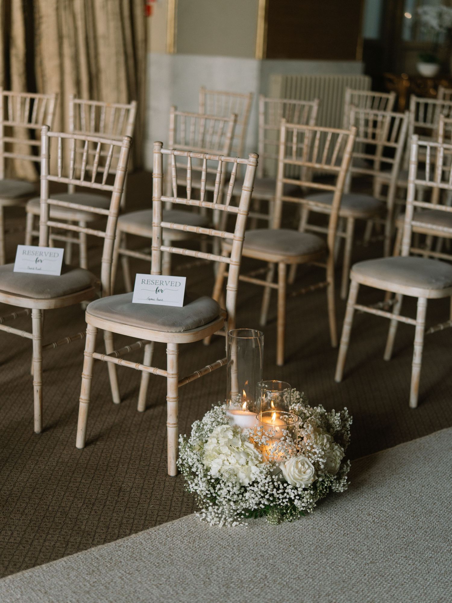 Elegant wedding ceremony setup with chiavari chairs, white floral wreath, and candlelight centerpiece on a gray aisle runner.