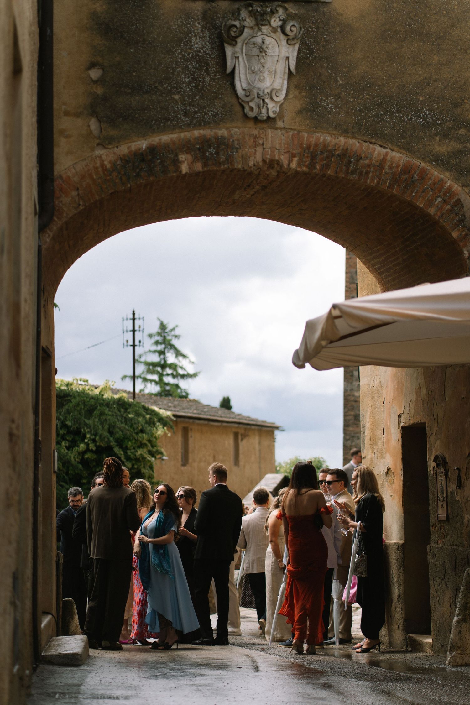 Wedding guests gathered under stone archway with heraldic crest at Italian villa venue.
