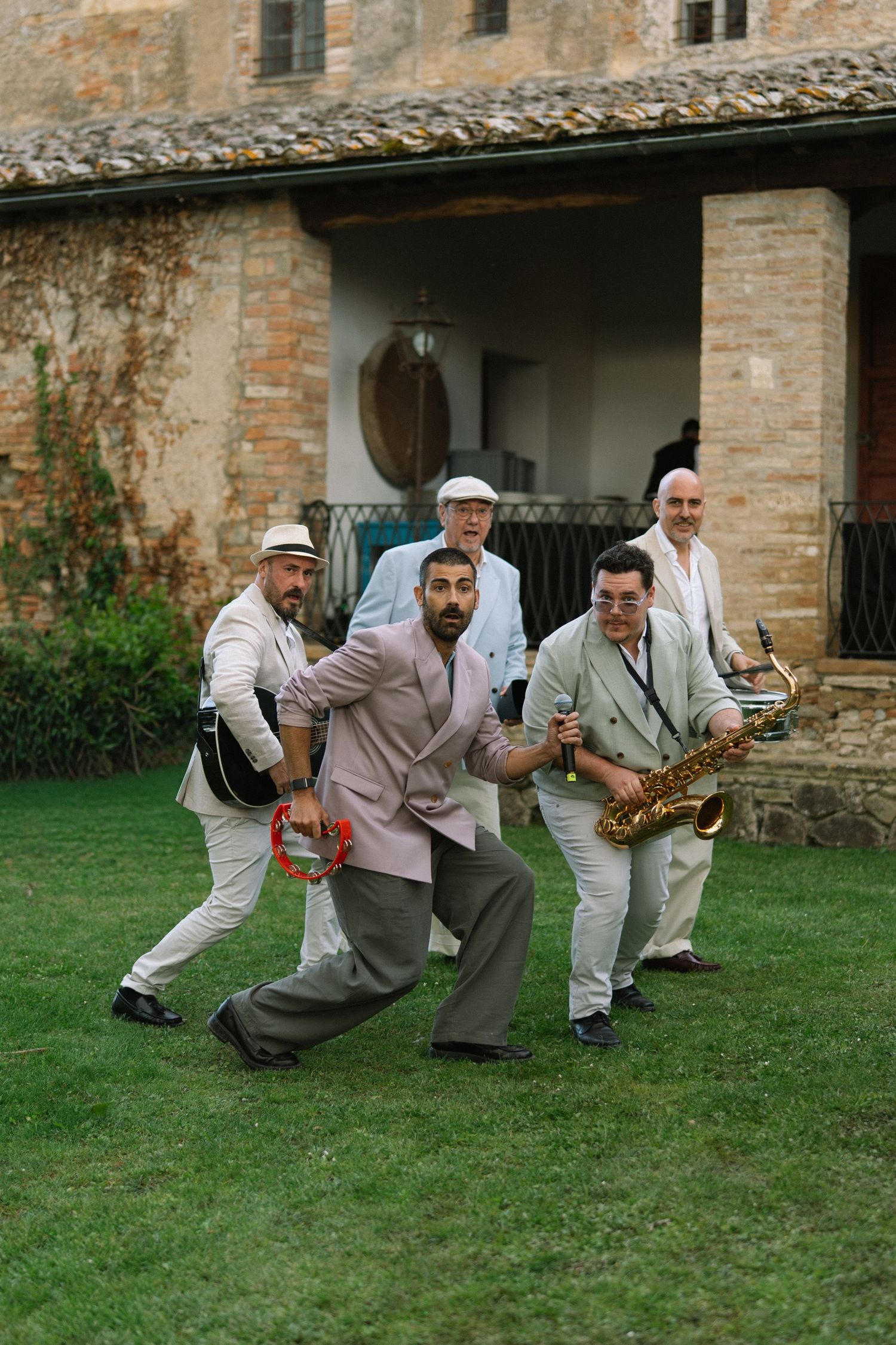 Lively jazz band with saxophone and guitar performing outdoors at a Tuscan villa wedding reception on green lawn.