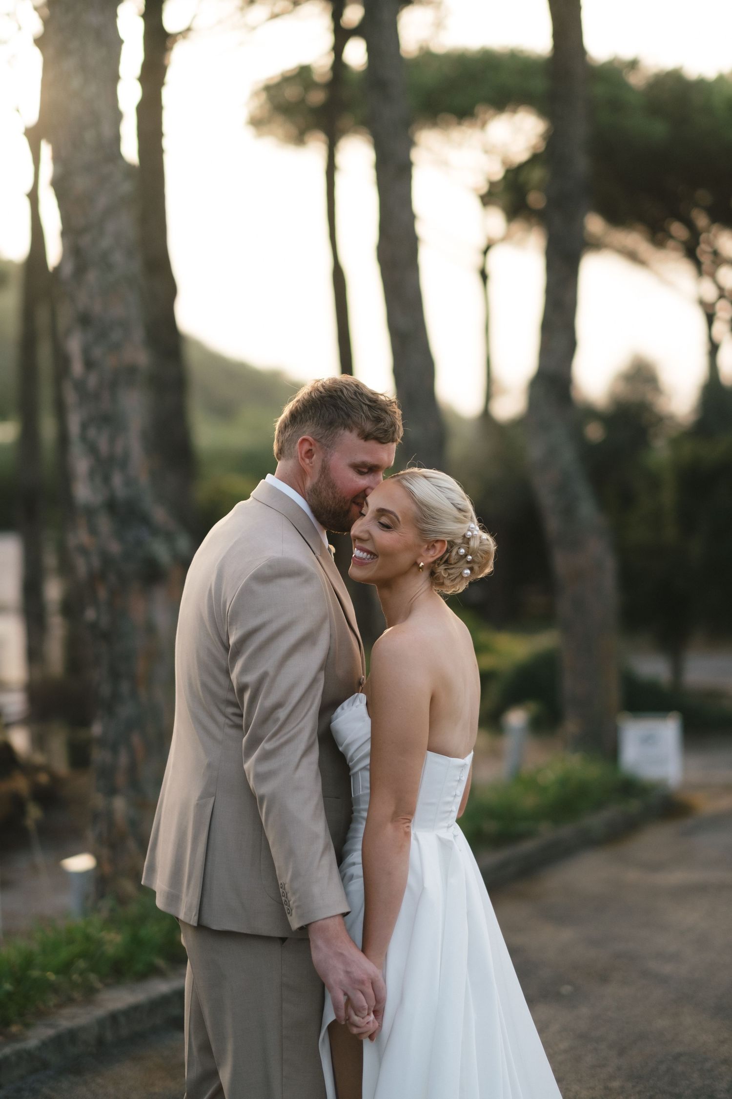Bride and groom embracing at sunset among tall pine trees at outdoor wedding.