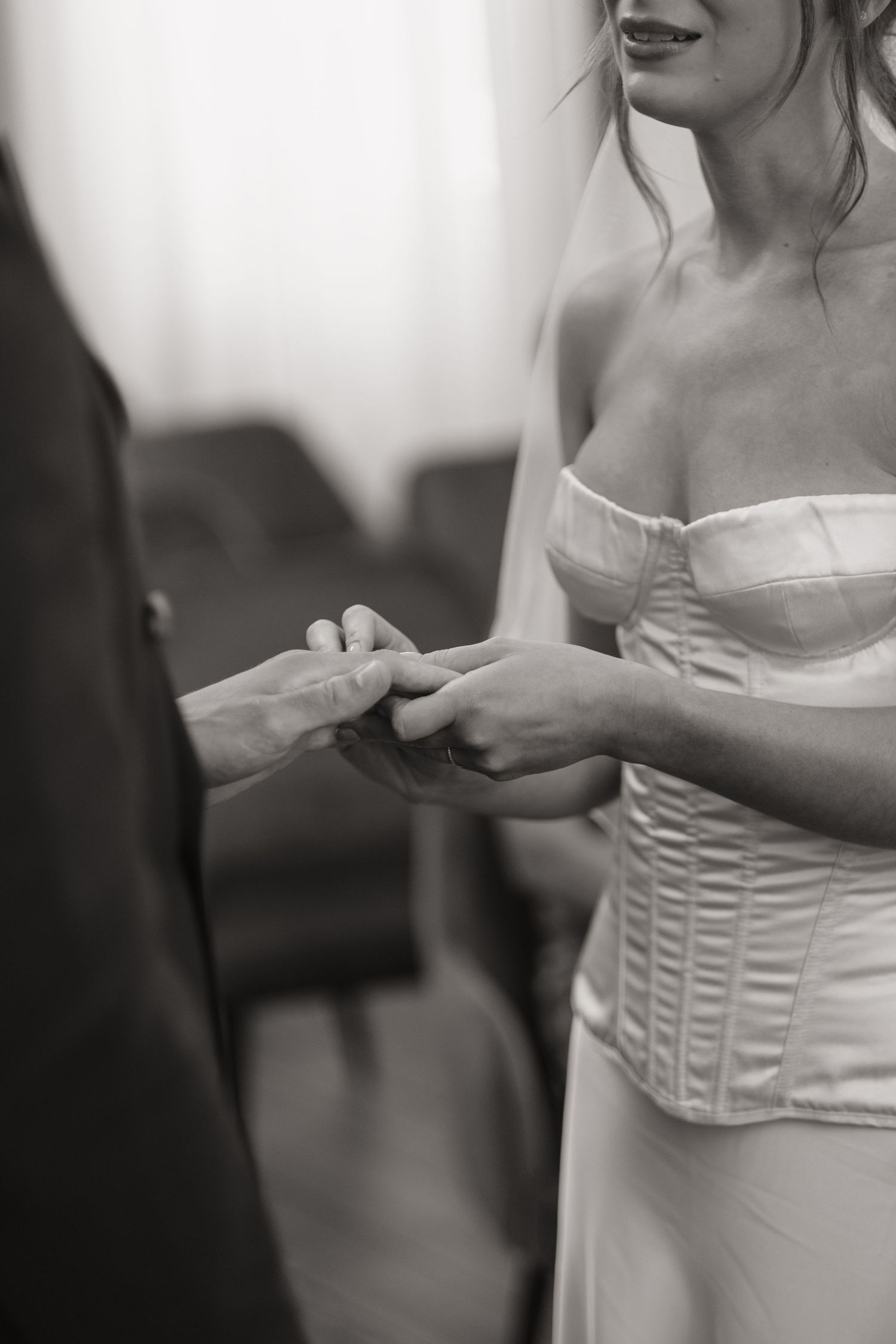 Black and white close-up of bride in strapless corset wedding dress exchanging rings with groom.