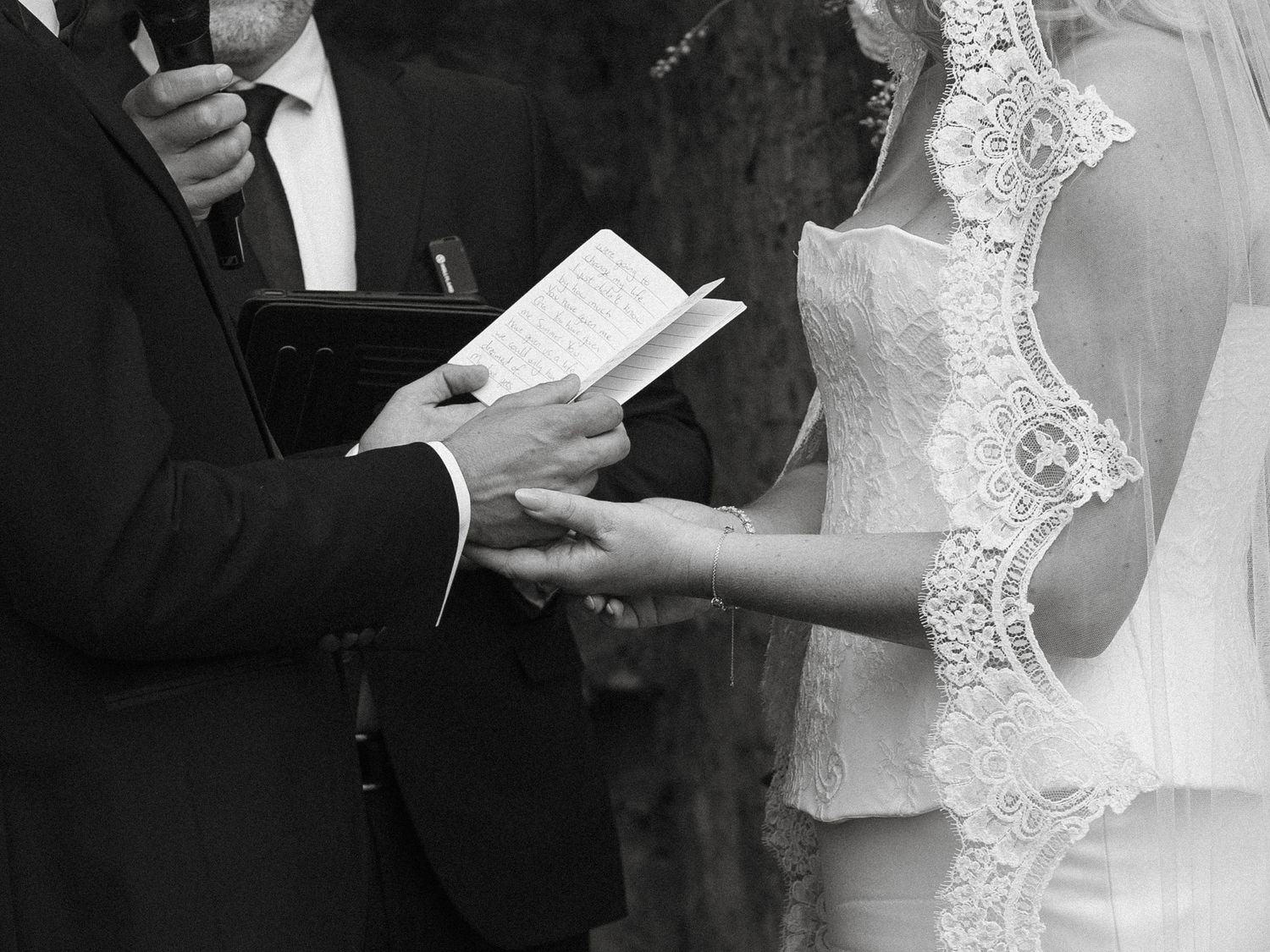 Black and white photo of bride and groom exchanging vows and rings during an outdoor wedding ceremony.