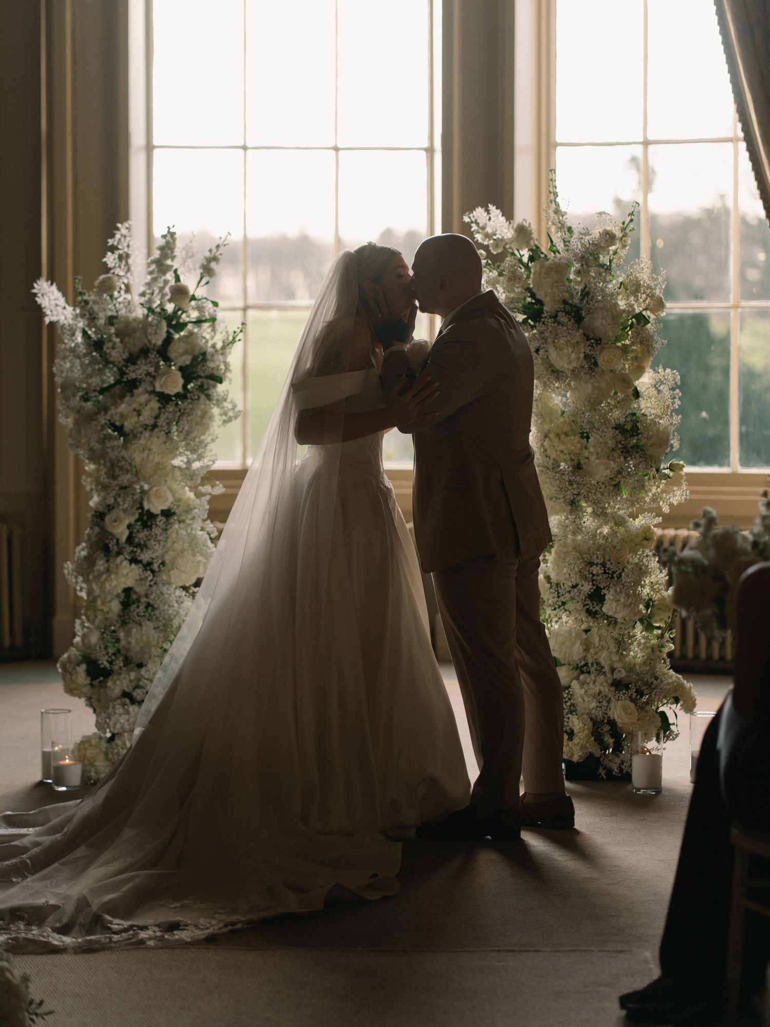 Bride and groom share a kiss at the altar framed by white floral arrangements in an elegant venue.