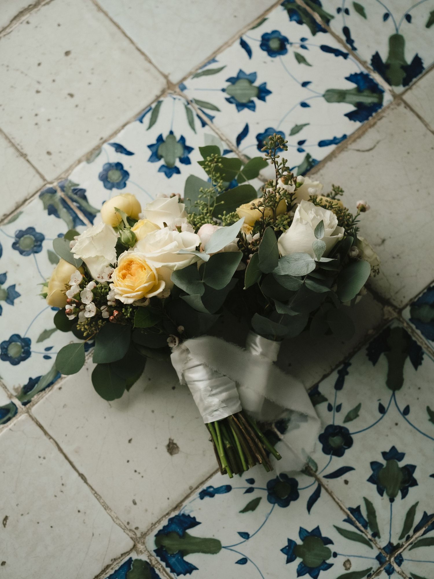 White and yellow rose wedding bouquet with eucalyptus on blue floral patterned tiles.