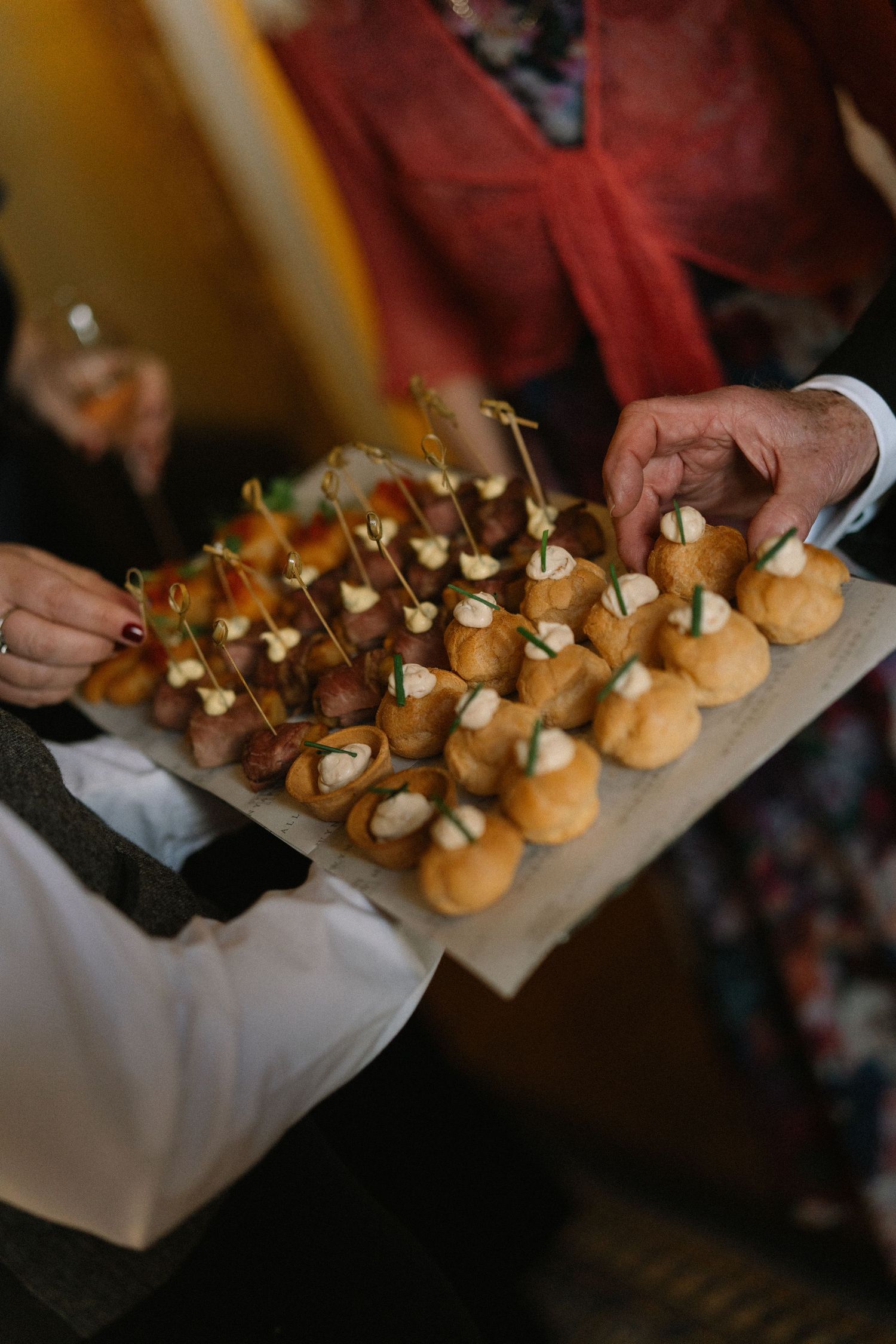 A server holds a tray of elegant bite-sized canapes with decorative picks at a catered event.