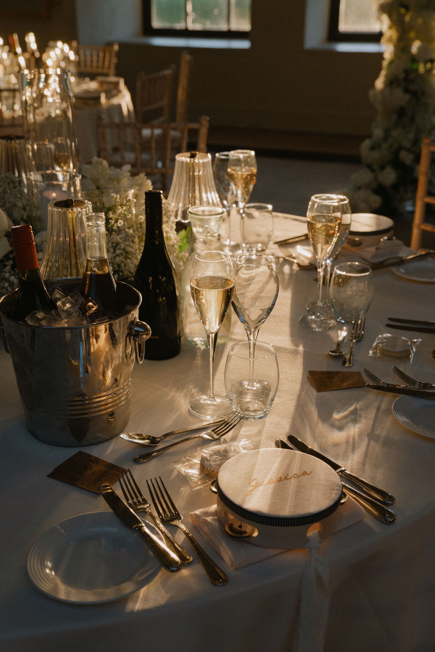Elegant wedding reception table setting with champagne flutes, gold cutlery, white linens, and wine bottles in ice bucket.