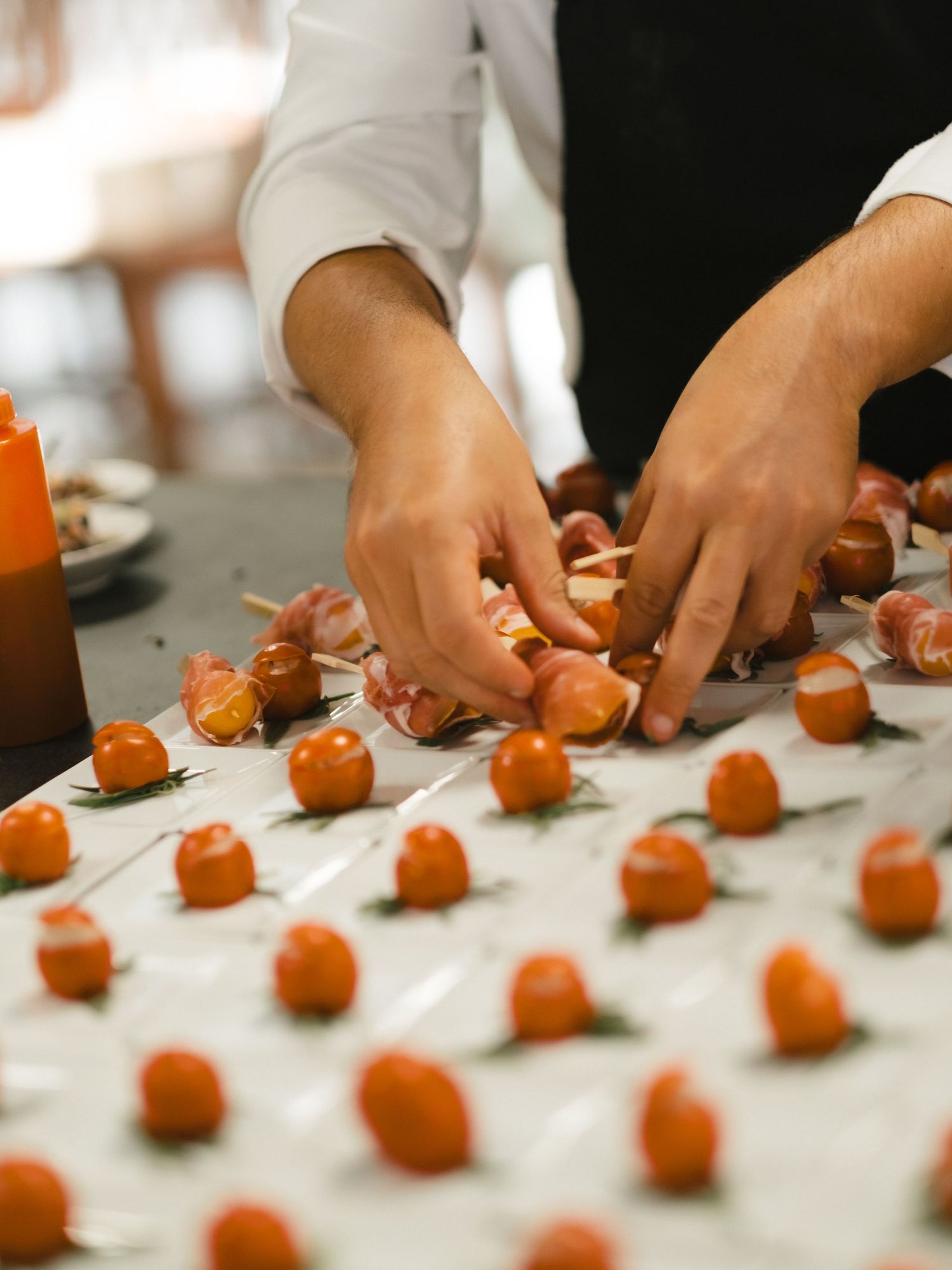 Chef carefully arranging prosciutto-wrapped cherry tomatoes appetizers on a white marble surface for an event.