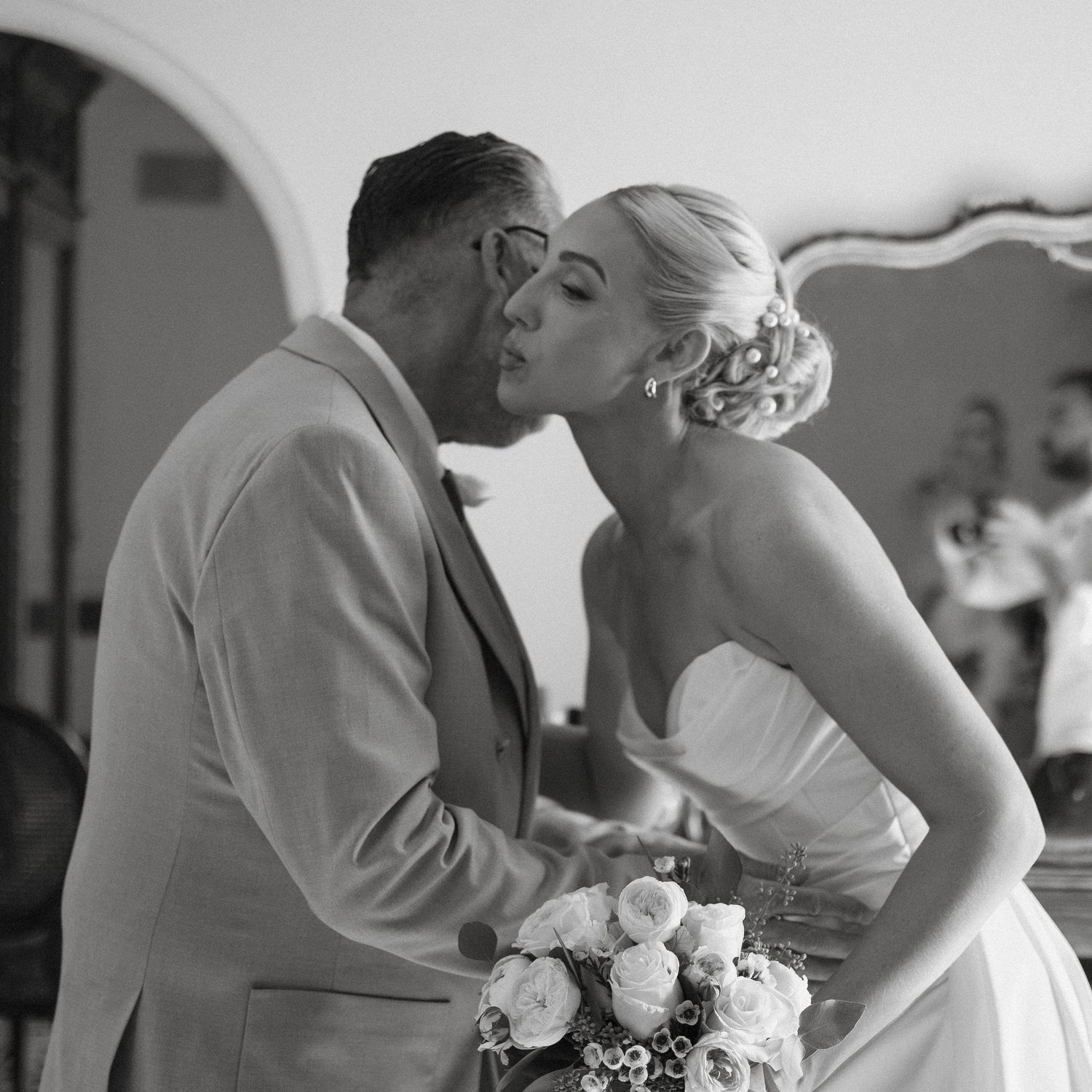 Black and white photo of a bride and groom sharing their first kiss at an elegant wedding ceremony.