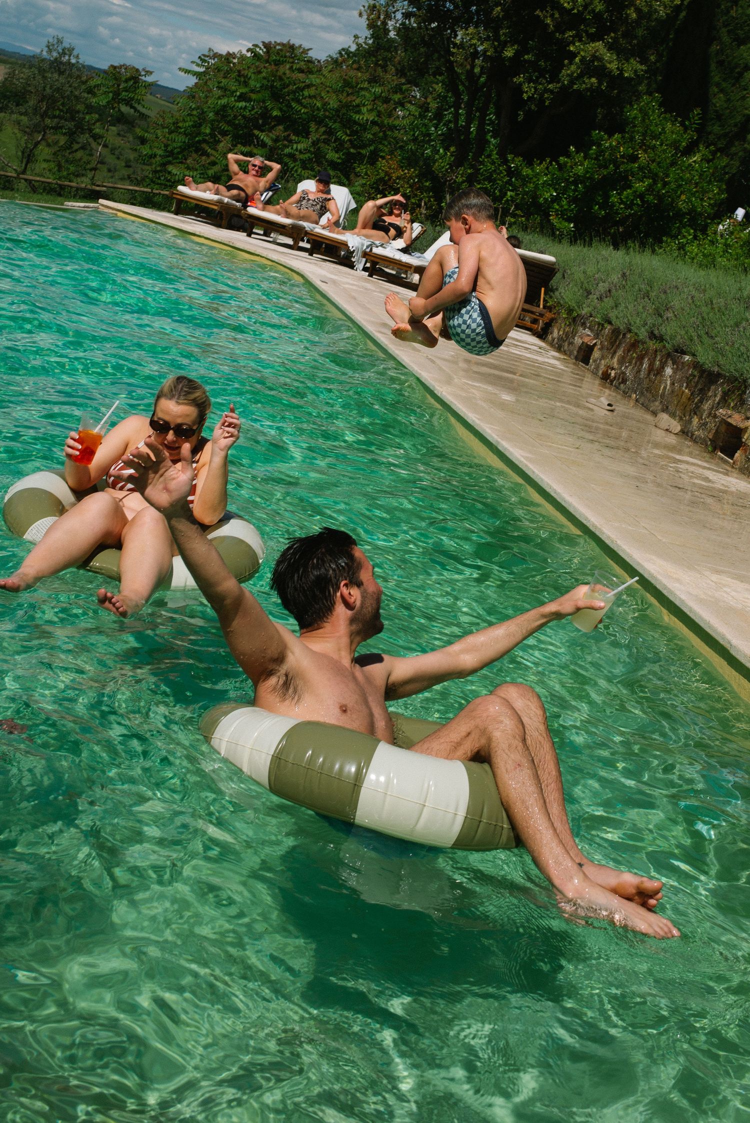 Guests relaxing on inflatable rings in a turquoise infinity pool in the Tuscan countryside.