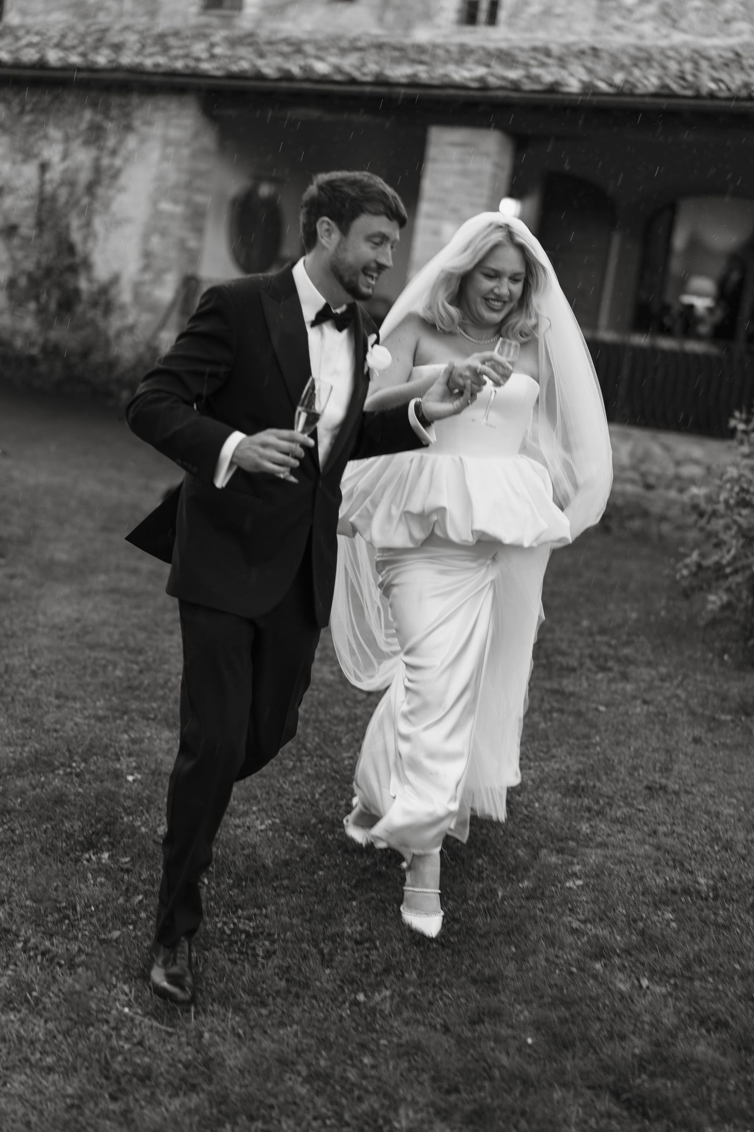 Black and white photo of laughing bride and groom running through garden at rustic Italian villa wedding.