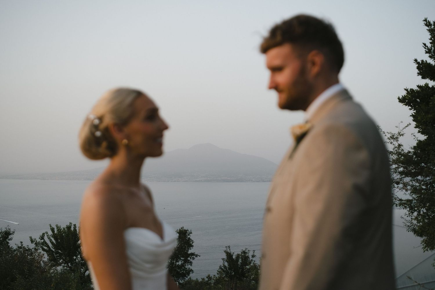 Bride and groom share romantic moment with mountain and sea backdrop at golden hour outdoor wedding.