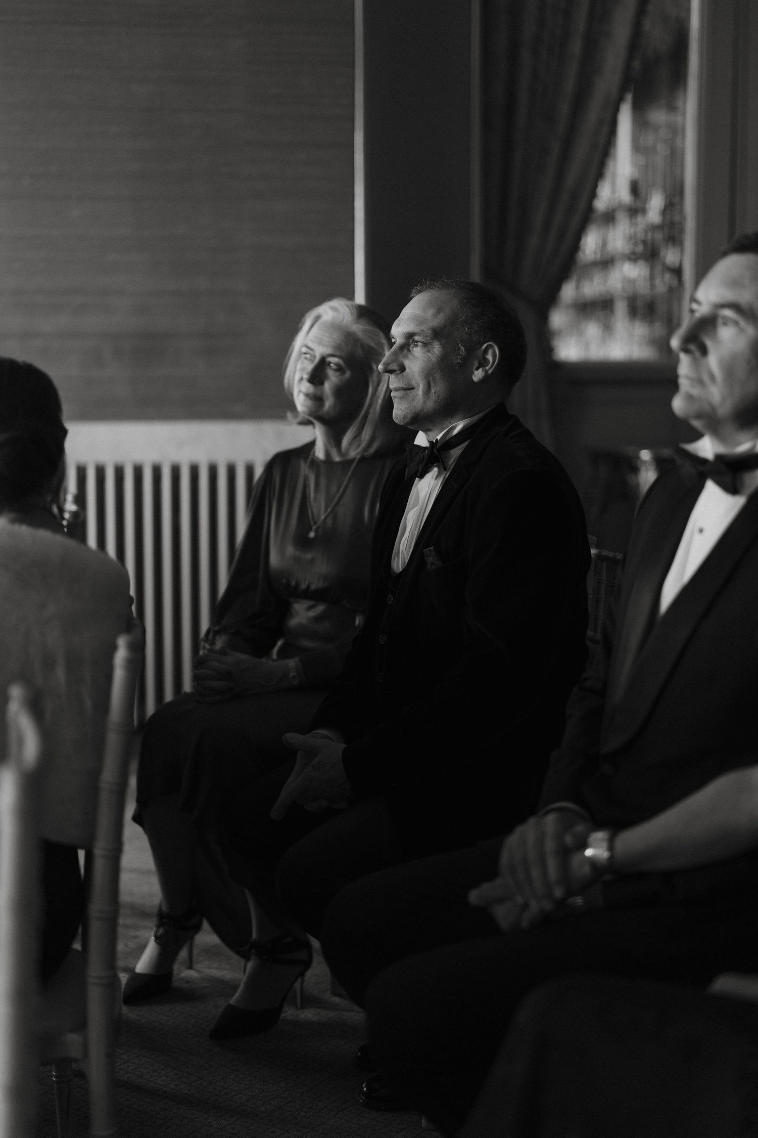 Elderly guests in formal attire seated at an elegant event, captured in black and white photography.