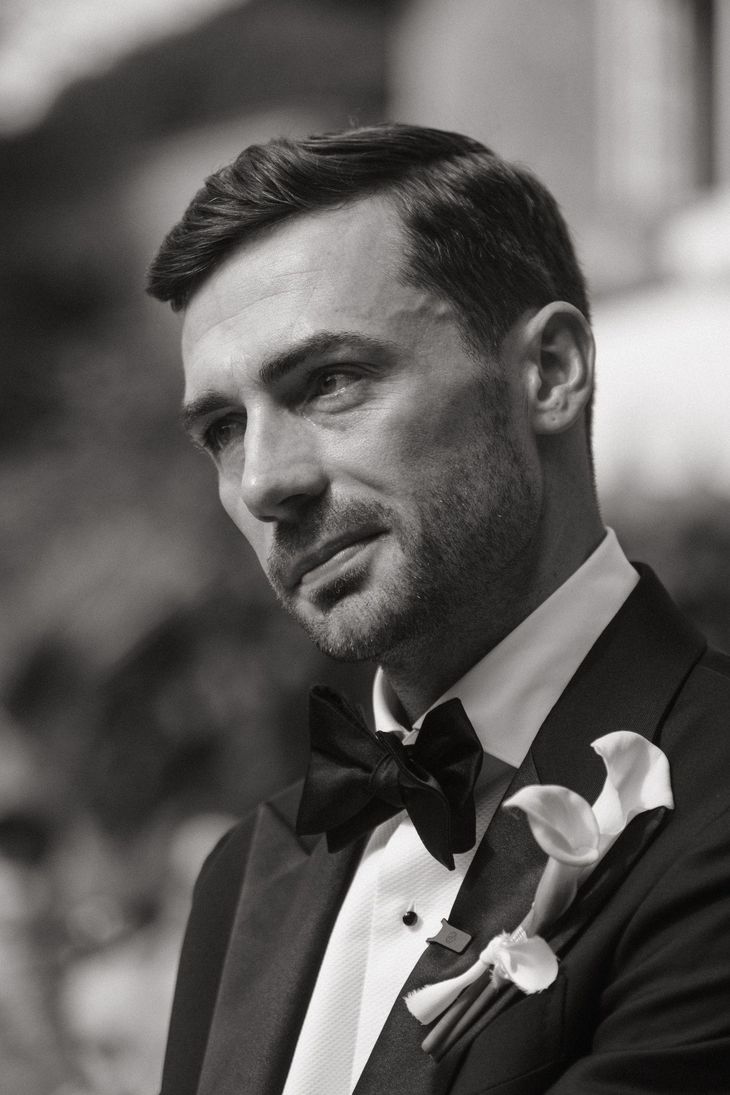 Black and white portrait of a groom in a tuxedo with bow tie and calla lily boutonniere.