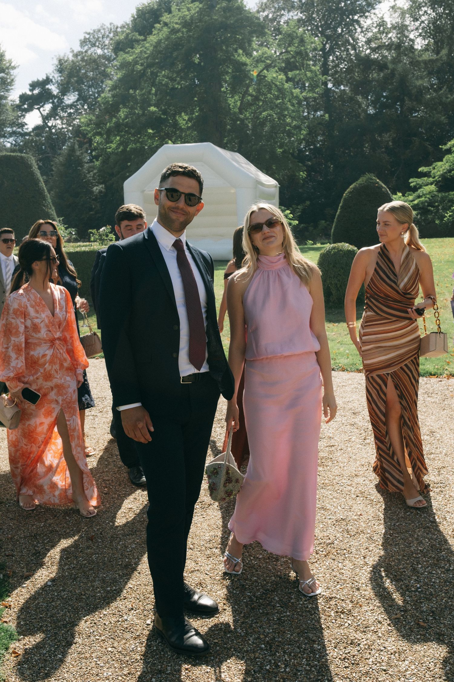 Elegant couple in formal attire posing at an outdoor garden wedding, woman in pink halter dress, man in dark suit with tie.