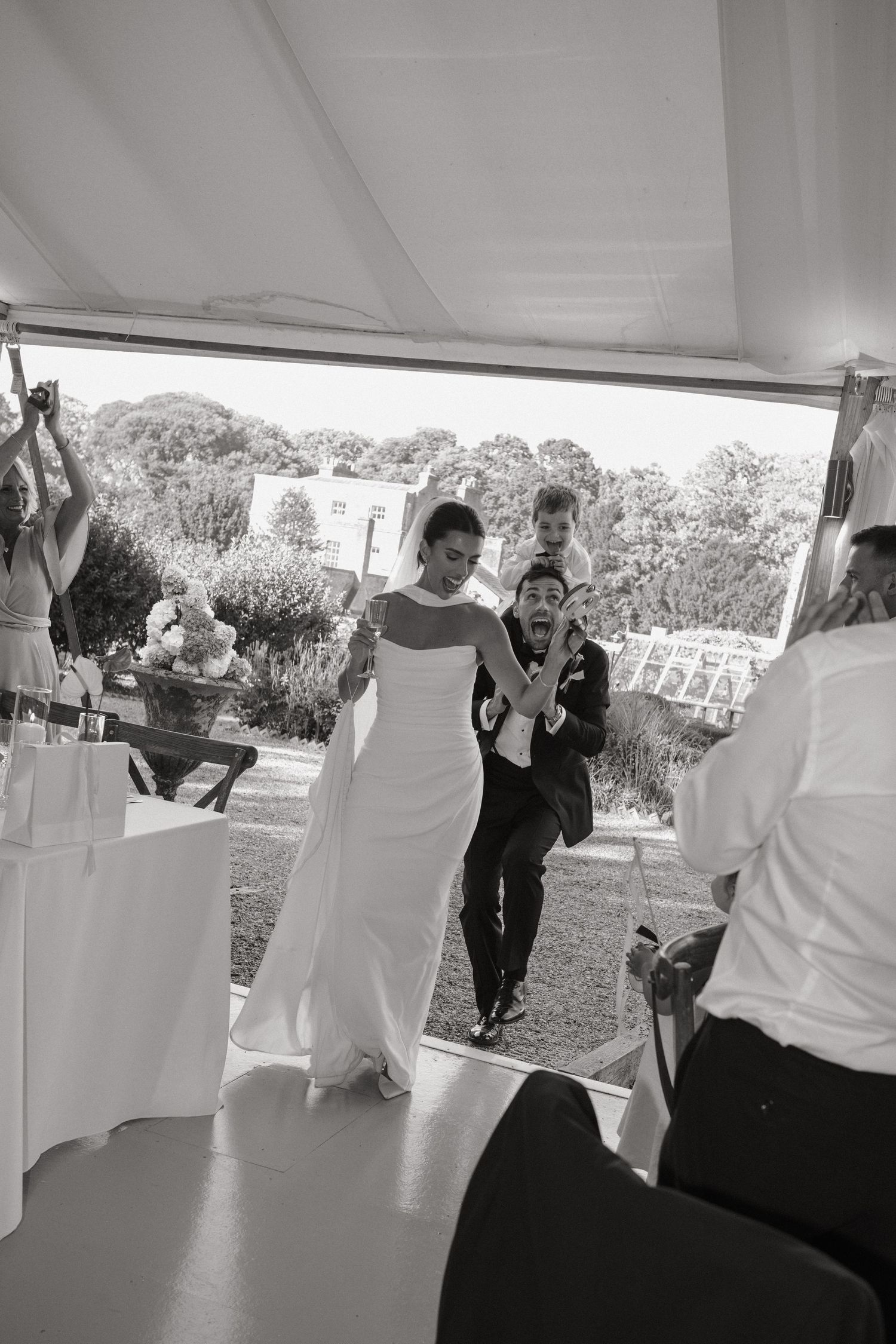 Black and white photo of a joyful bride and groom making their grand entrance at an outdoor wedding reception.