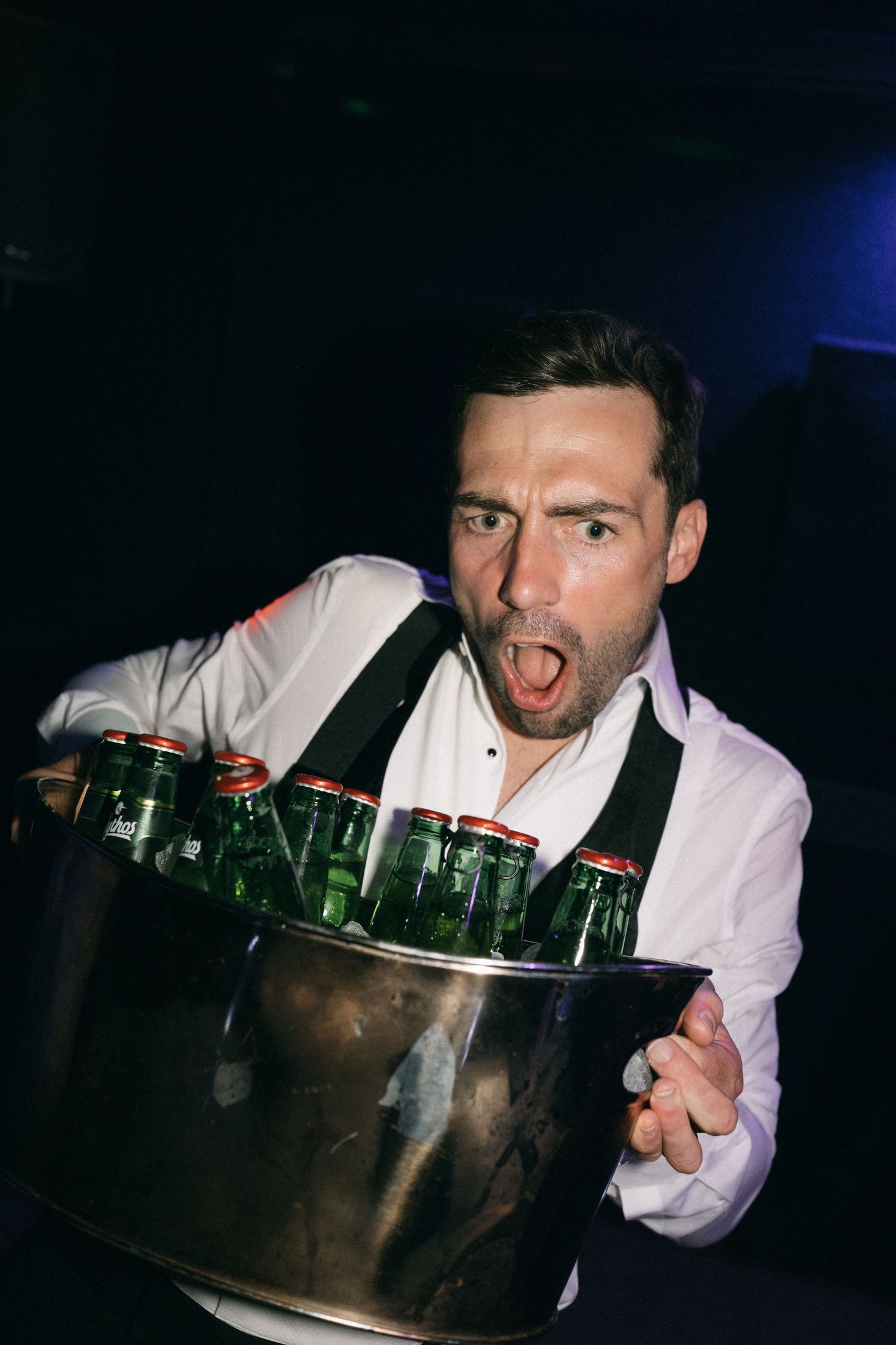 A bartender holds a metal bucket filled with green glass bottles at a nightclub event.