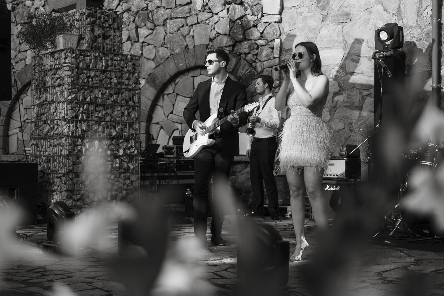 Black and white photo of a live band performing, guitarist and female singer at an outdoor venue.