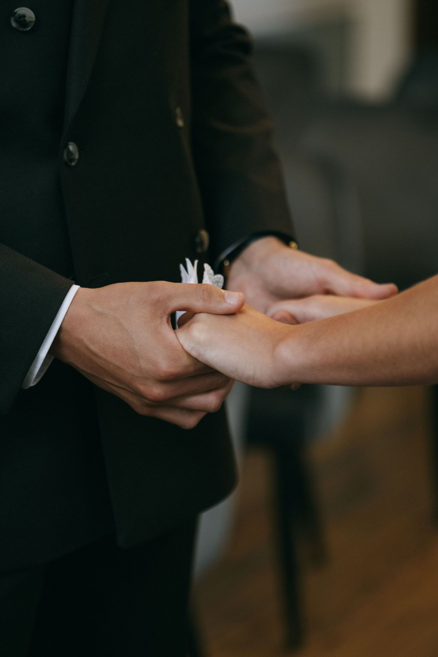 Close-up of groom placing wedding ring on bride's hand during ceremony, wearing black suit with white pocket square.
