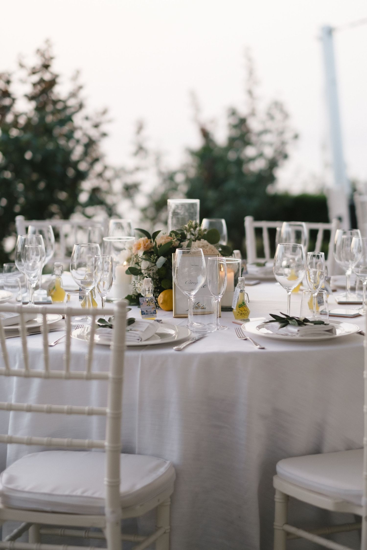 Elegant outdoor wedding reception table set with white linens, floral centerpiece, candles and glassware.